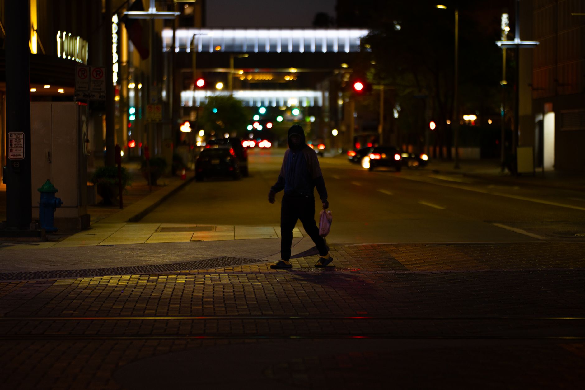 A person crosses a dimly lit street in downtown Houston at night.