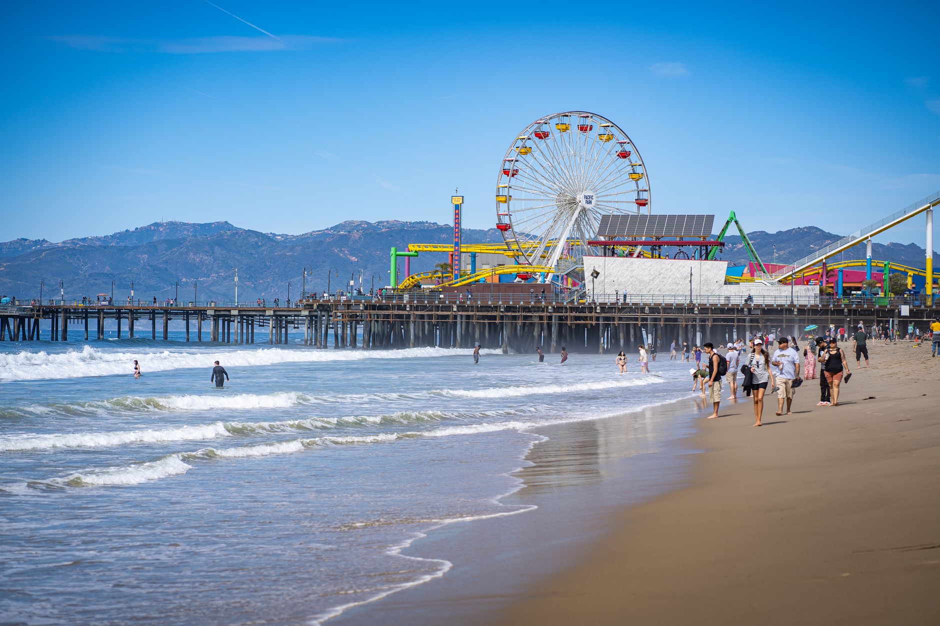 Scenic view of Santa Monica Pier with Ferris wheel, beach, and people enjoying a sunny day.