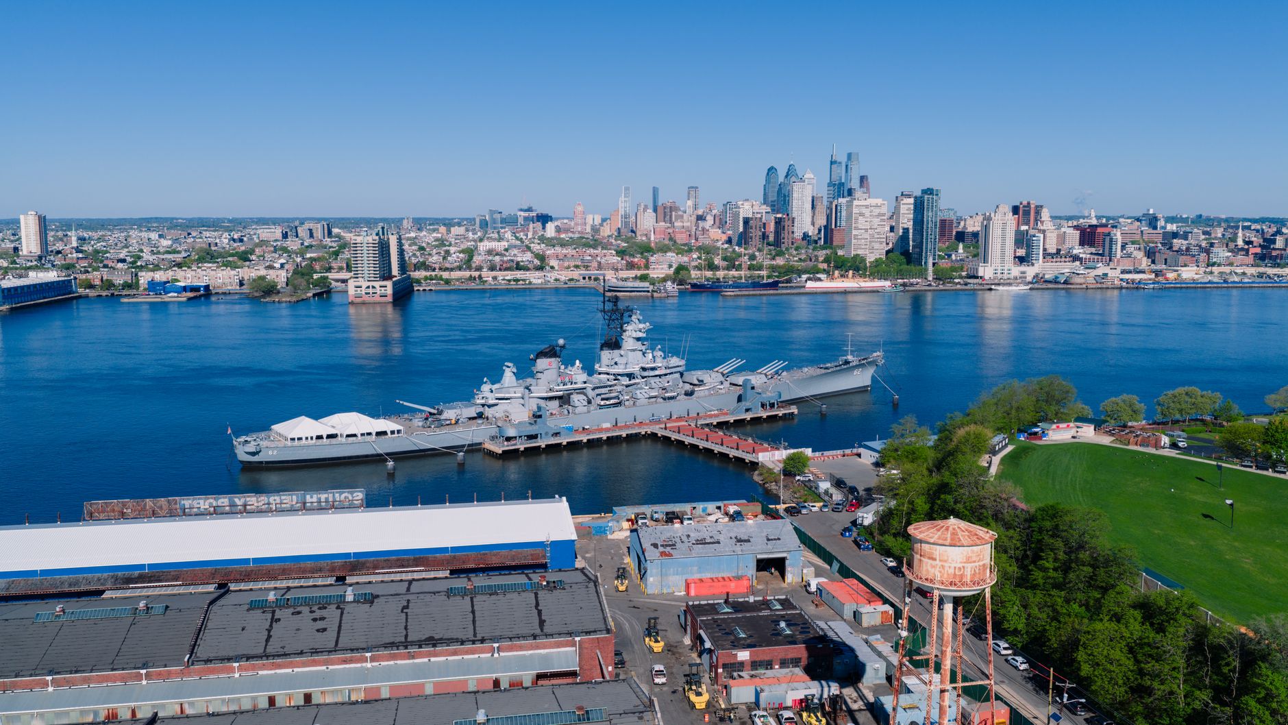 Stunning aerial view of Philadelphia skyline and moored battleship over blue river.
