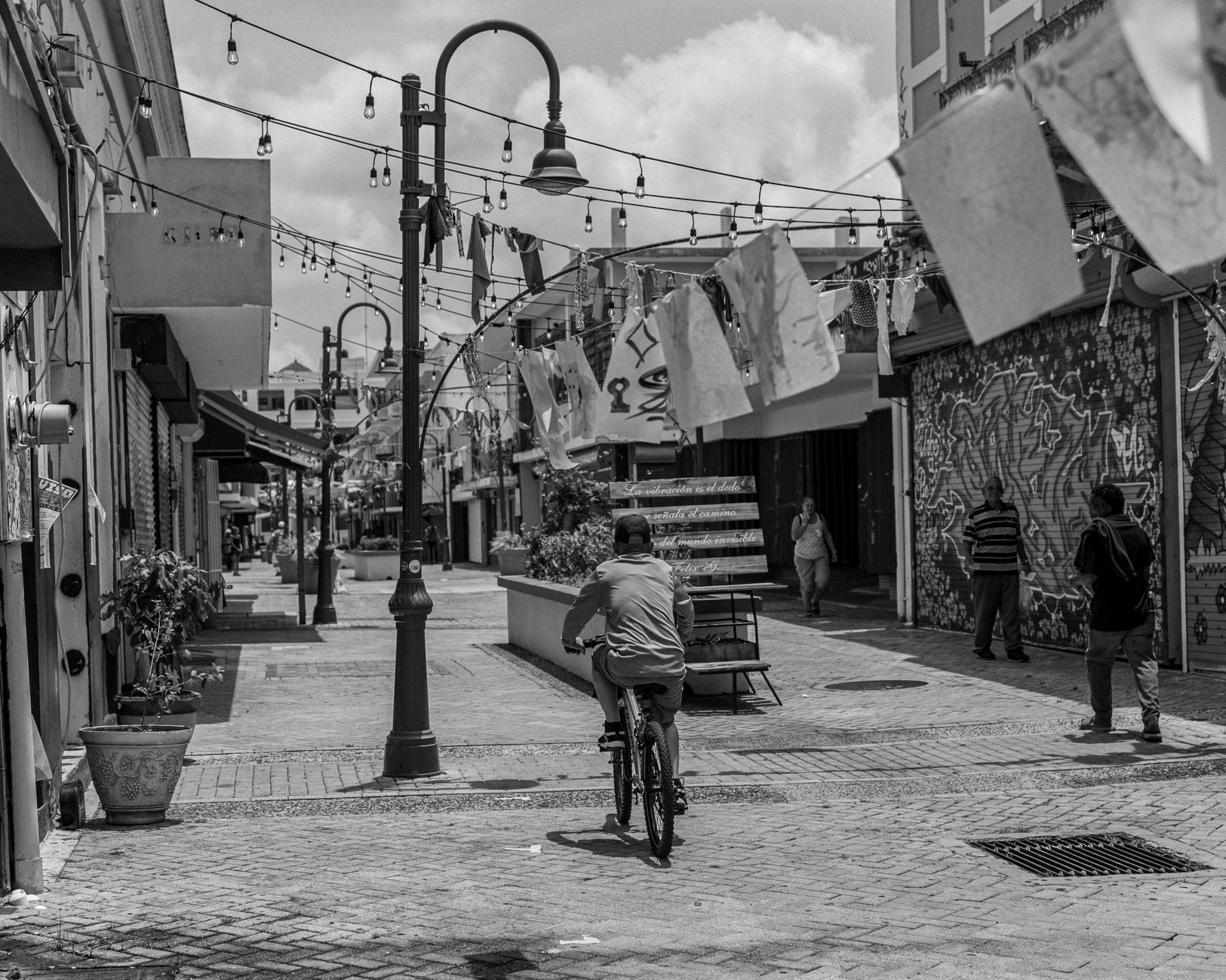 A cyclist rides through an artistic alley in Caguas, Puerto Rico, with hanging decorations and street art.