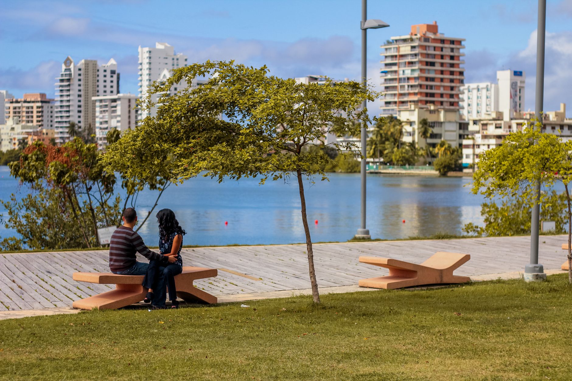 A couple enjoys time together on a bench in a vibrant urban park by the waterfront.