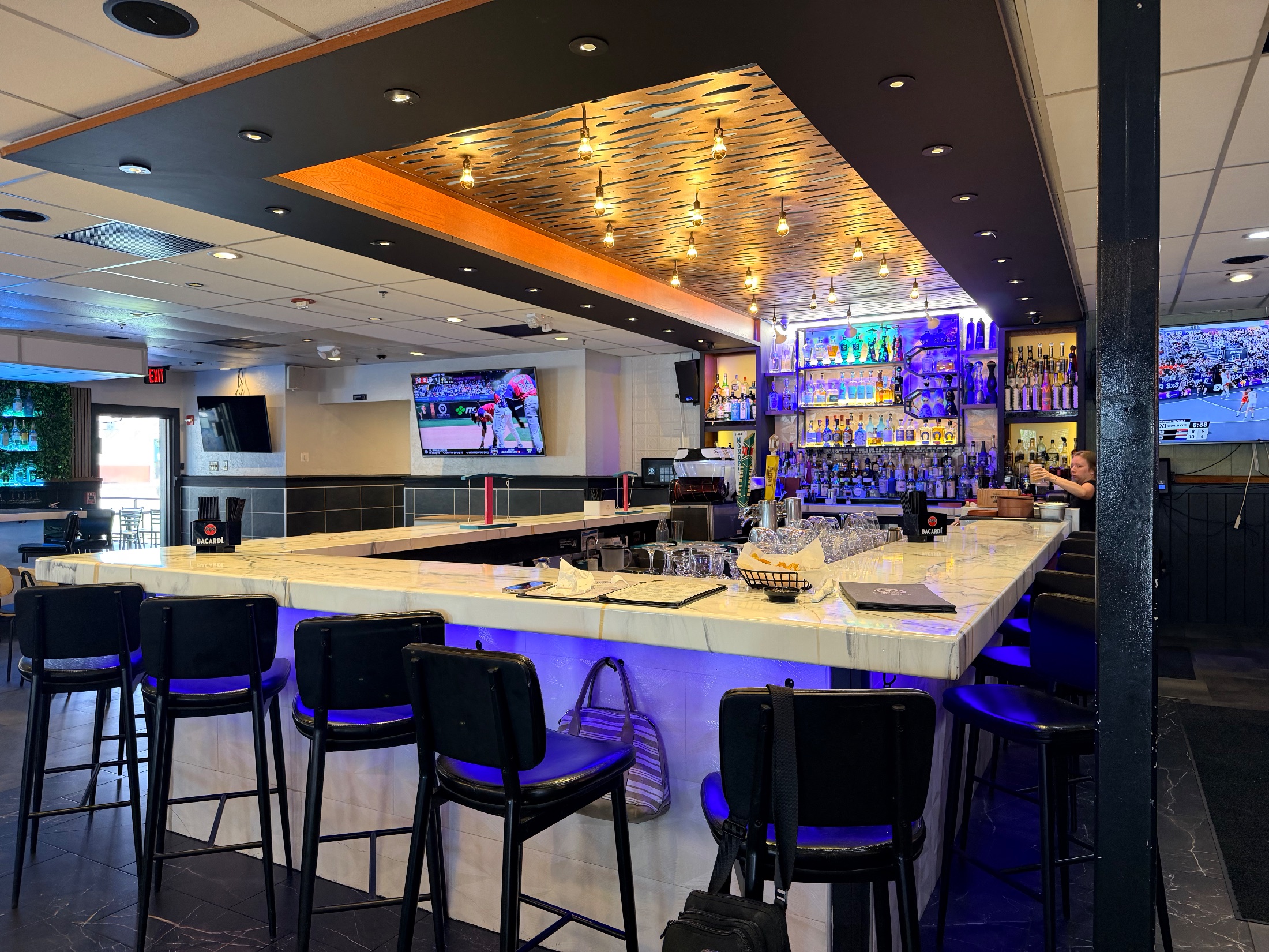 Wide marble bar at Fiesta Azul with blue LED lighting, full liquor shelves, and pendant lights overhead