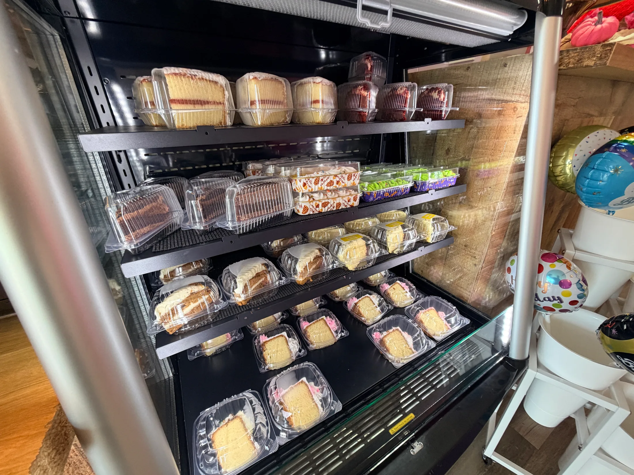 Grab-and-go cake slices packed in clear plastic containers stacked across multiple shelves at Brenda's Cake Shop