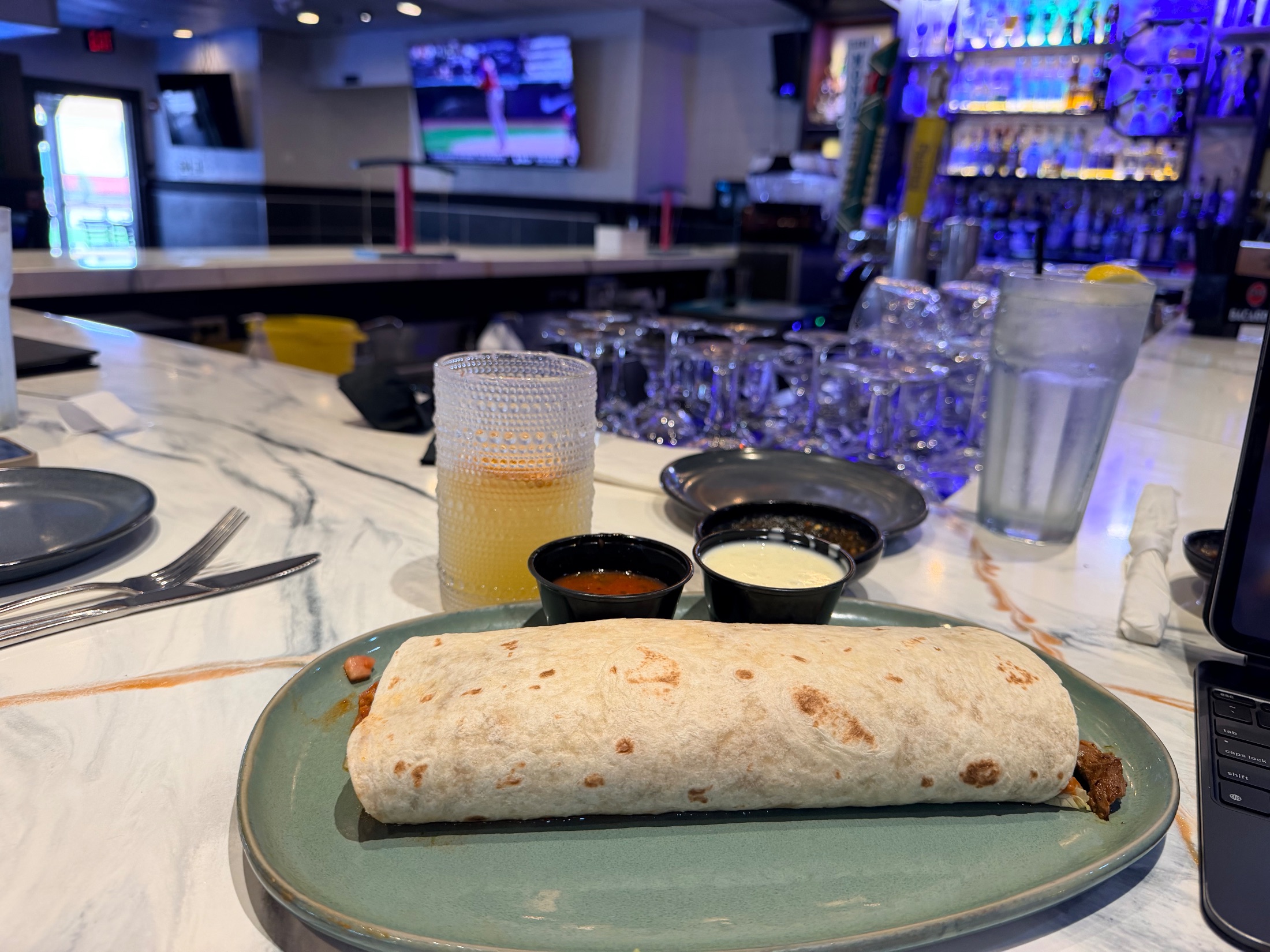 Steak burrito on a teal plate with two dipping sauces and a house margarita at the Fiesta Azul bar