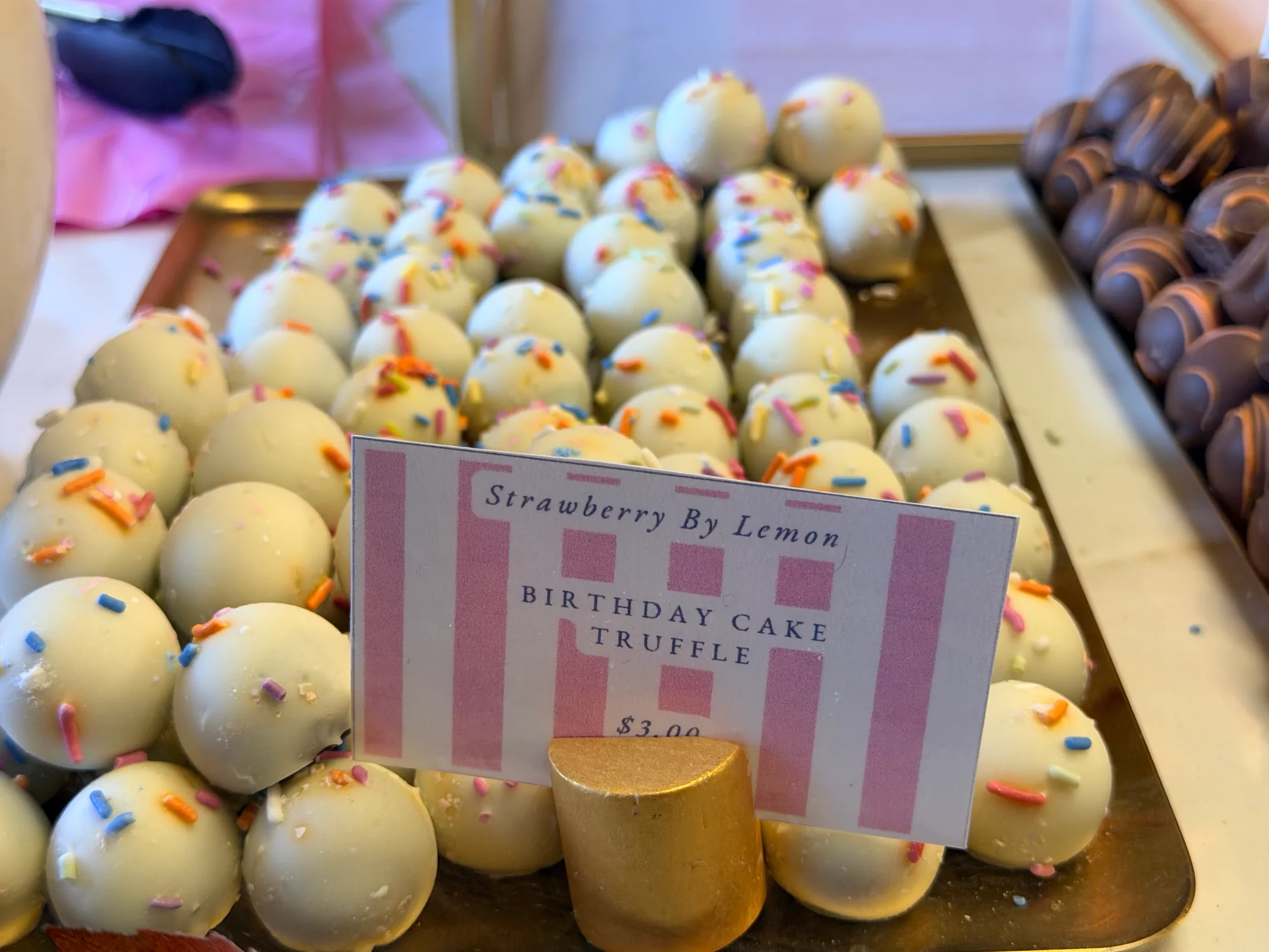 A tray of Birthday Cake Truffles from Strawberry by Lemon, white chocolate with rainbow sprinkles, priced at $3.00 each