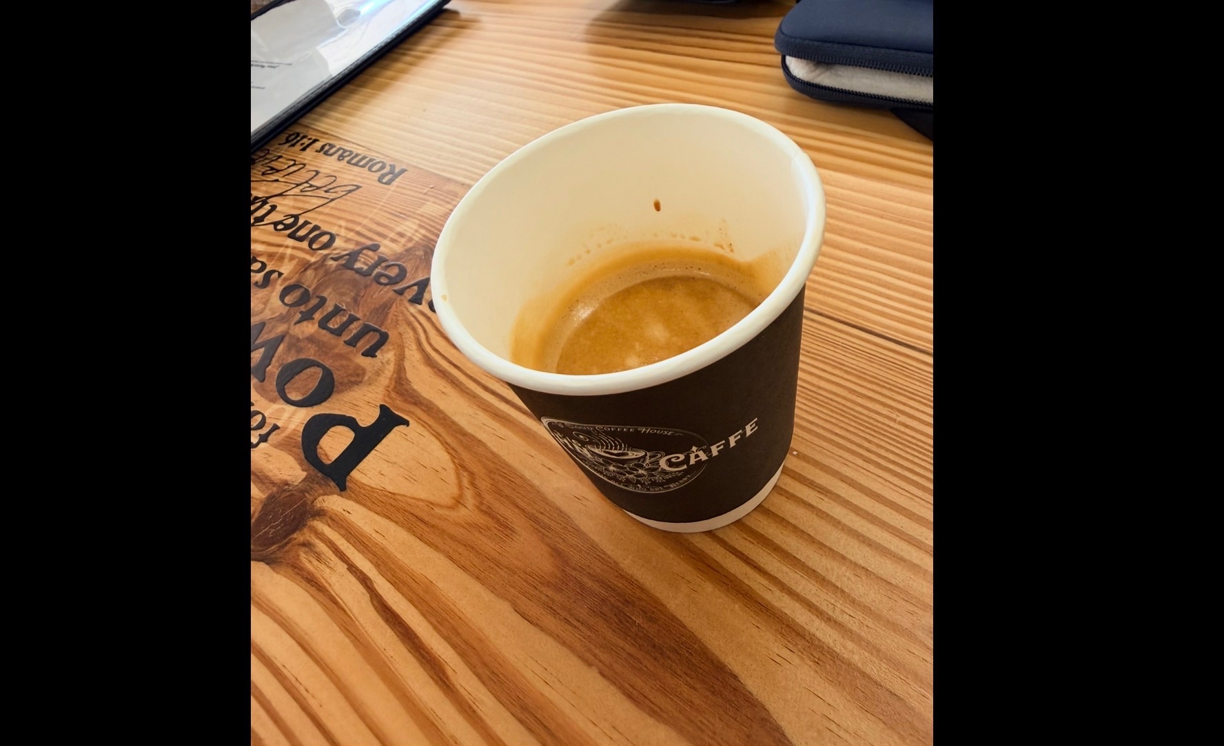 A John 3:16 Caffe branded espresso cup resting on a wood-etched table, with a golden crema visible at the rim