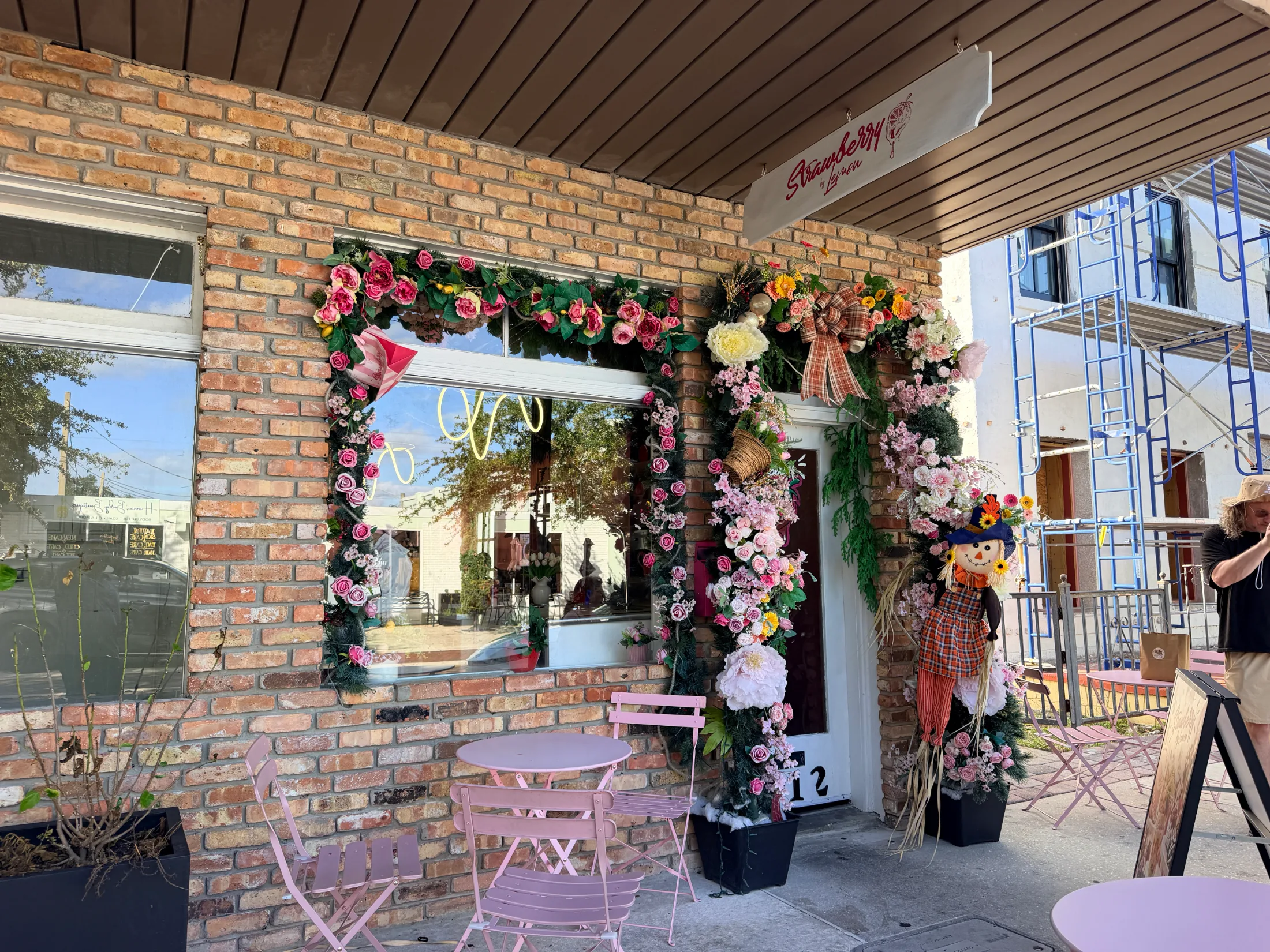 The flower-framed exterior of Strawberry by Lemon on New York Avenue in St. Cloud, Florida, with pink bistro chairs on the sidewalk
