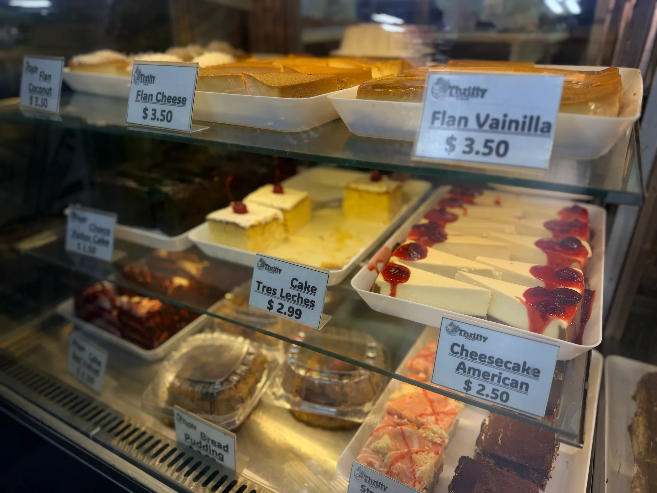 Bakery dessert case showing flan coconut, flan cheese, flan vainilla, tres leches cake, cheesecake, and other sweets at Thrifty
