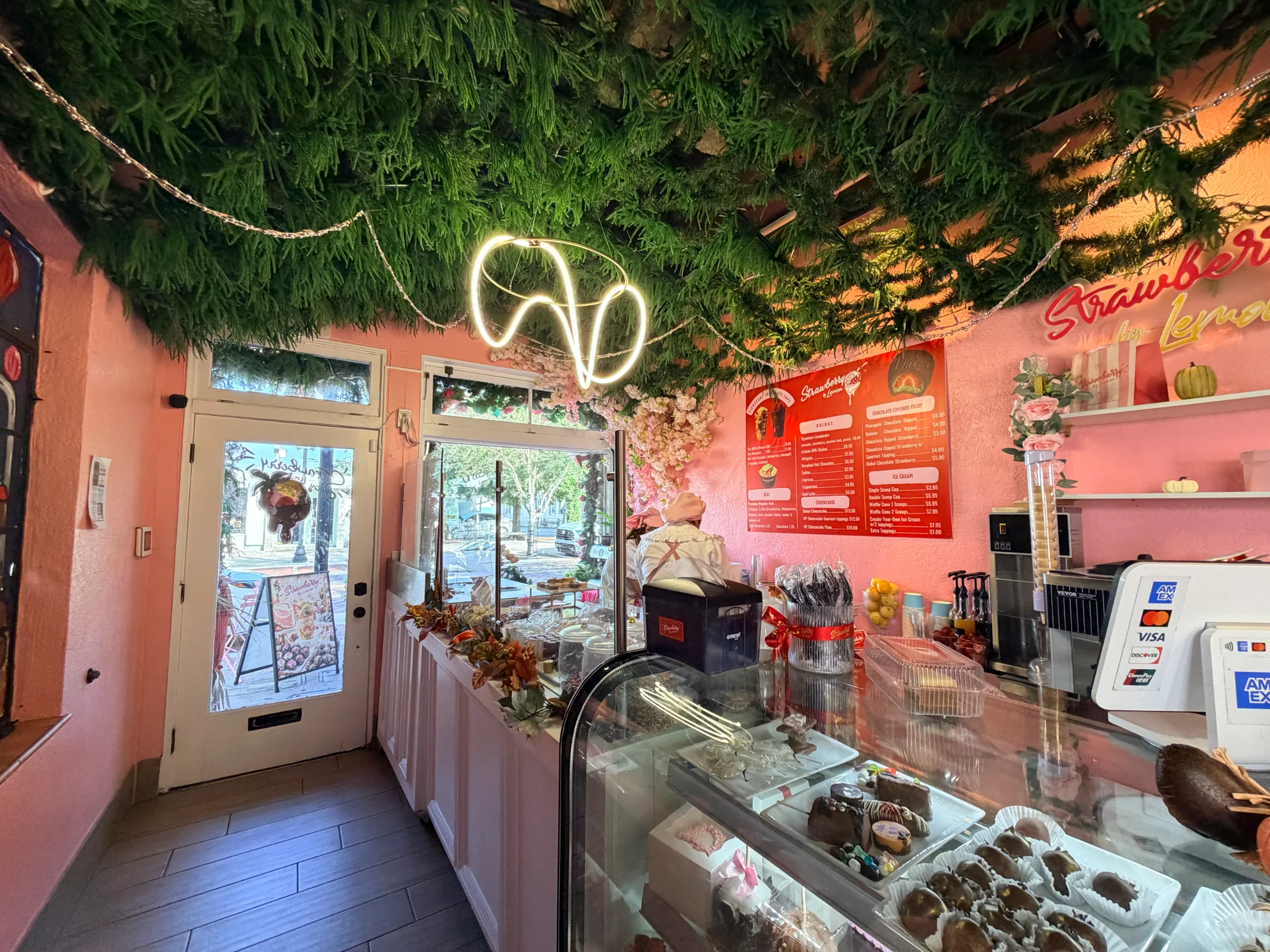 Interior of Strawberry by Lemon showing pink walls, a greenery ceiling, neon ice cream cone sign, and the display counter