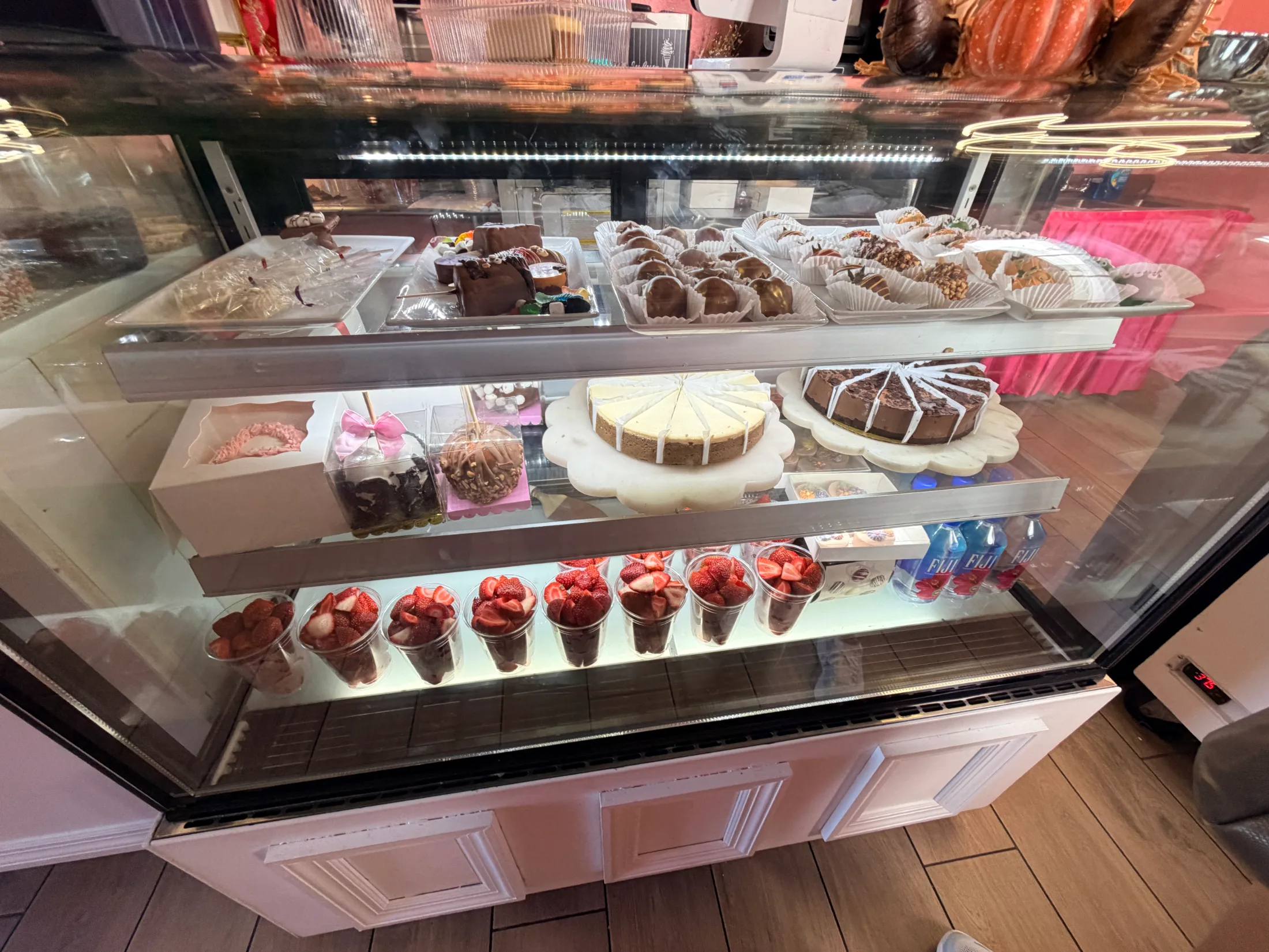 The full display case at Strawberry by Lemon showing Dubai strawberry cups, cheesecakes, chocolate bonbons, and other treats