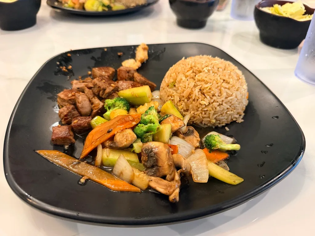 Steak hibachi plate with broccoli, mushrooms, carrots, and fried rice on black ceramic