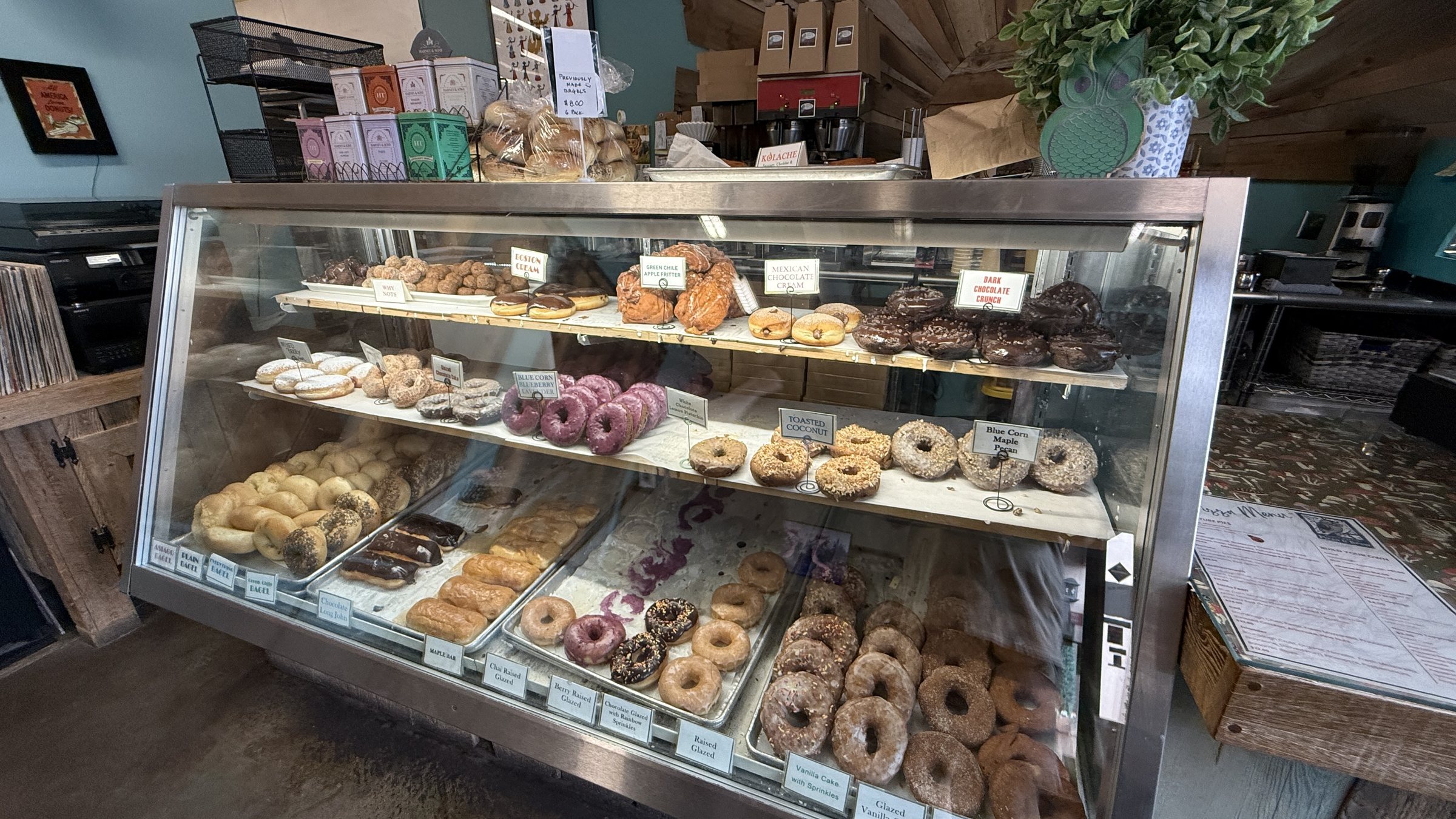 A glass case of donuts at Whoo's Donuts, with glazed rings, sprinkled donuts and purple glazed donuts on trays