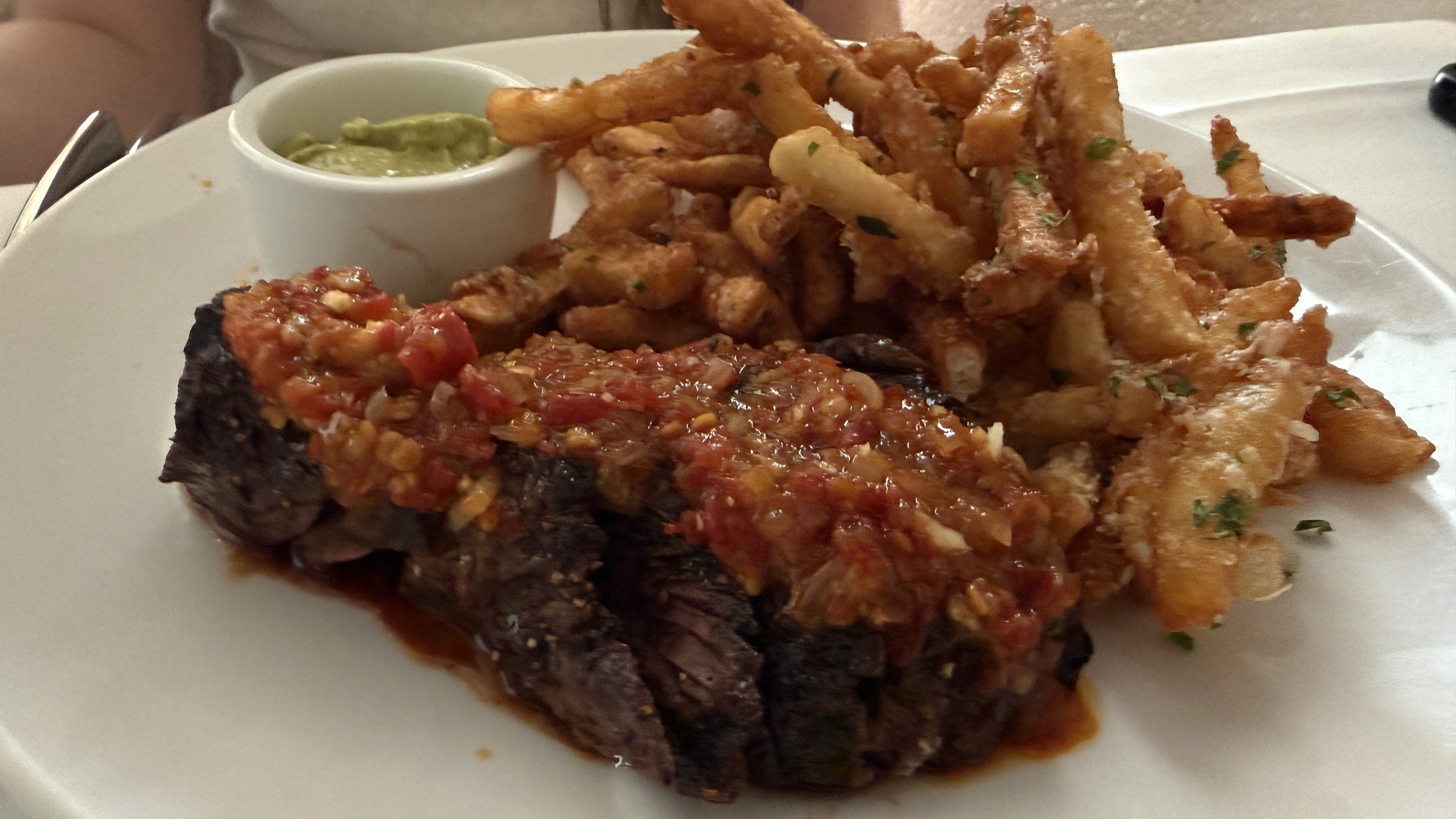 A sliced hanger steak topped with red chimichurri next to a pile of fries and a small cup of green sauce