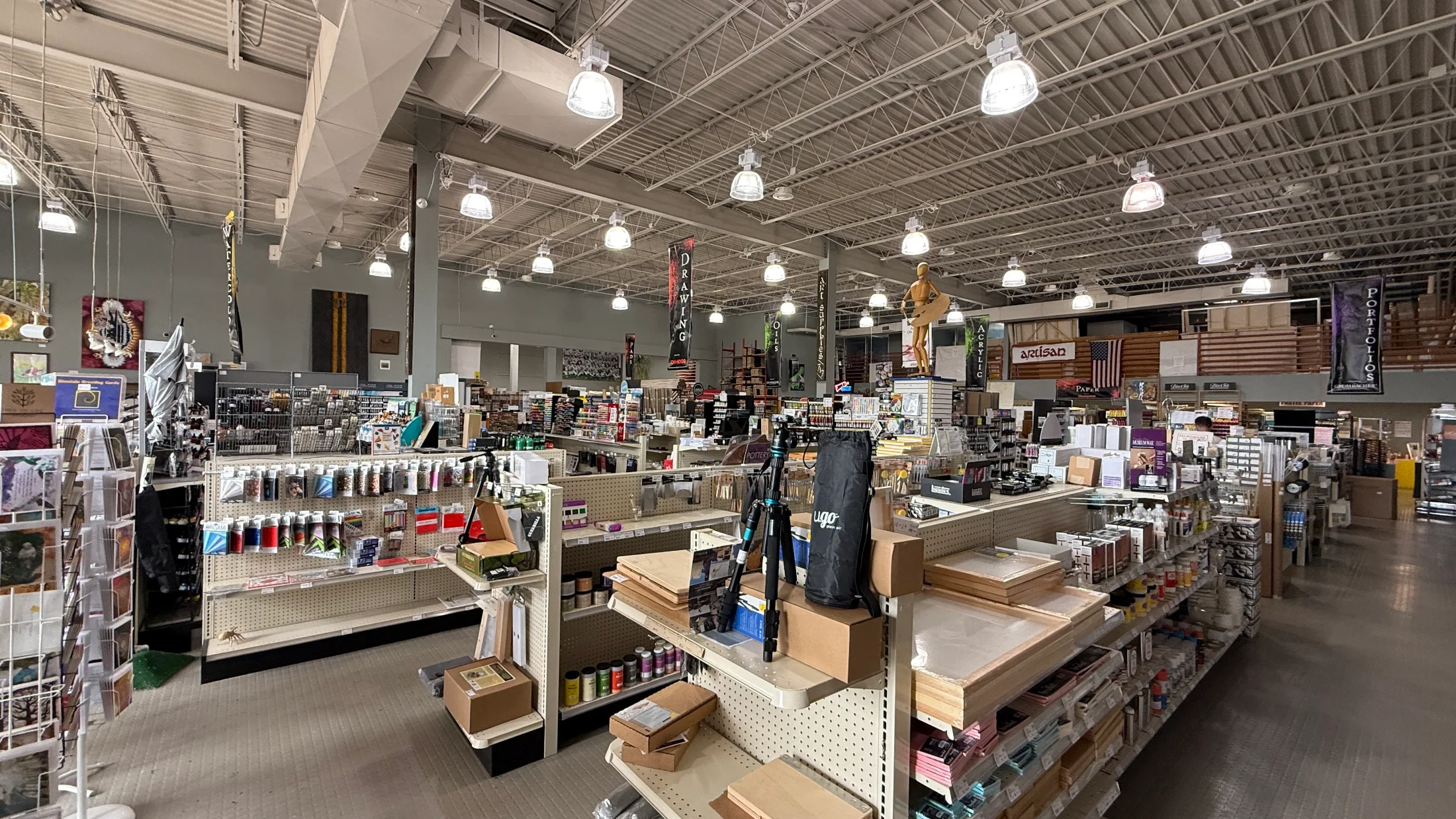 Wide view of Artisan Santa Fe's sales floor showing aisles of art supplies beneath hanging department banners