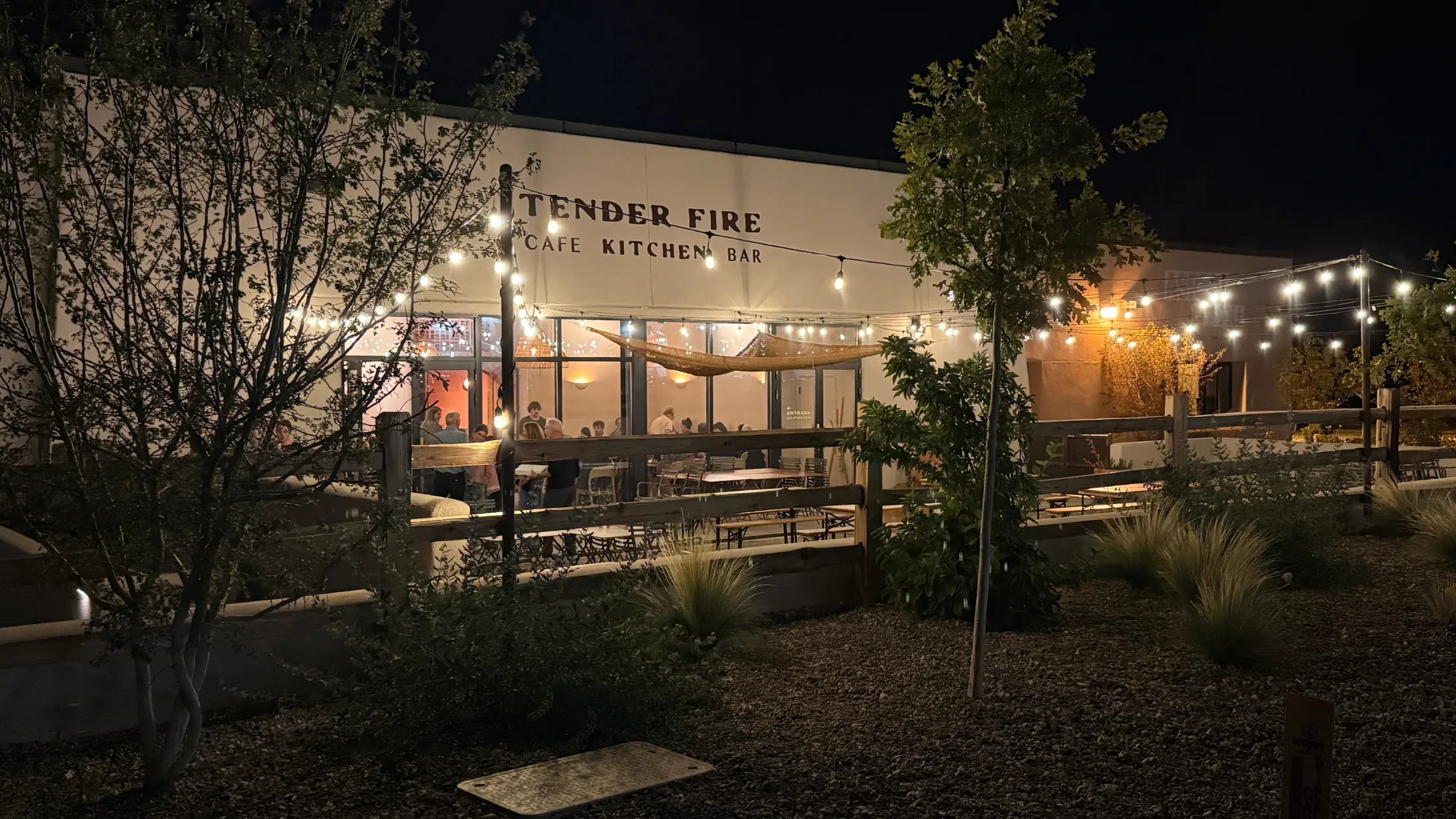 Tender Fire Cafe Kitchen Bar patio at night, string lights over outdoor seating, guests dining inside