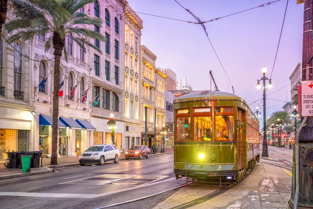 New Orleans streetcar glowing amber at dusk on Canal Street, palm trees and Beaux-Arts buildings lining the corridor