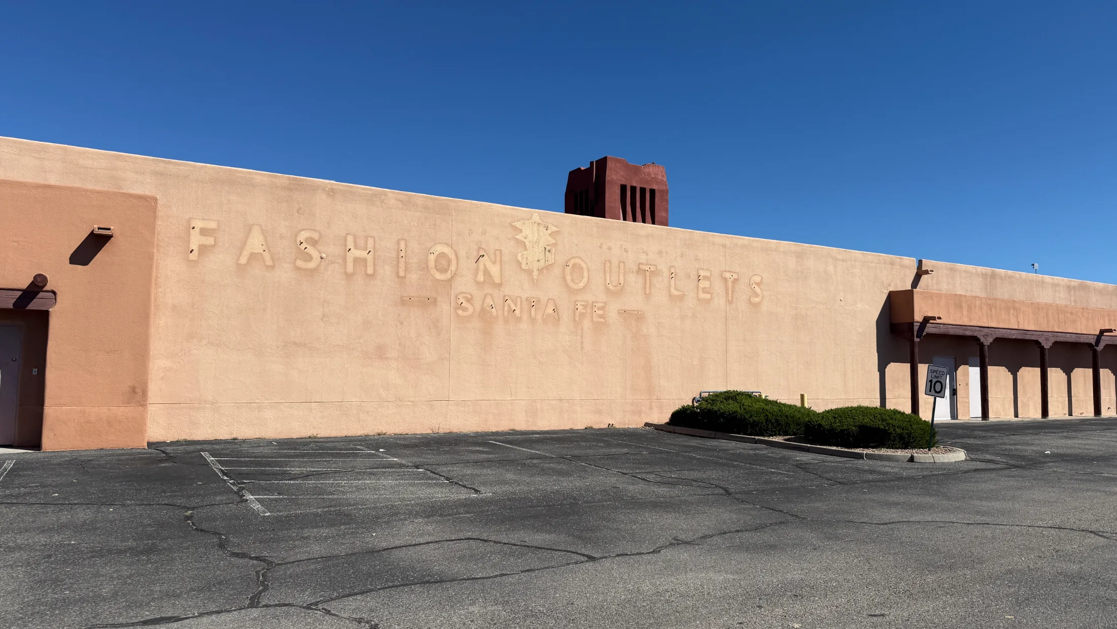 Ghost lettering reading Fashion Outlets Santa Fe still pressed into the stucco exterior wall, with the property's red tower visible above