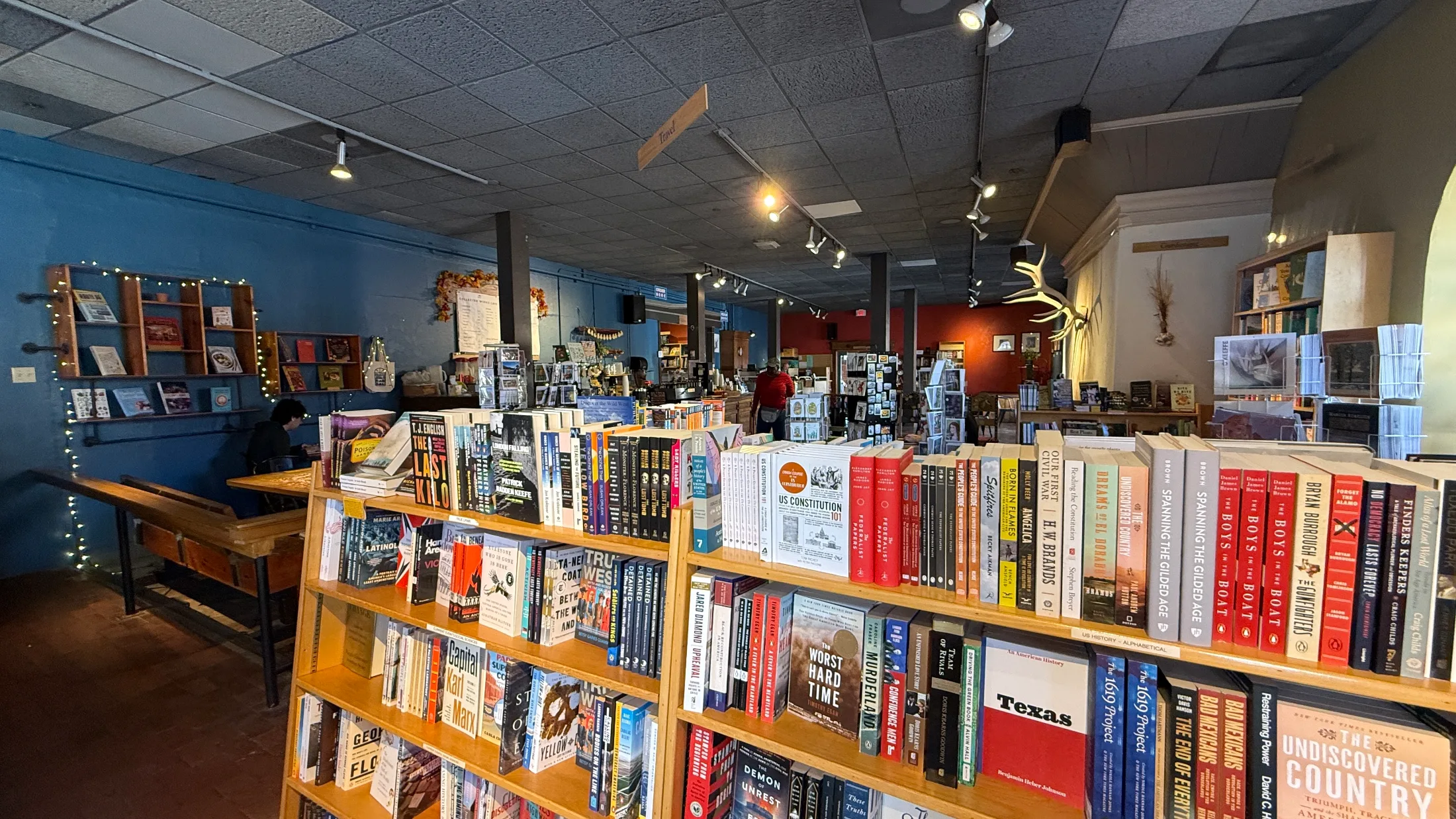 Interior shelves at Collected Works showing Travel section, US History alphabetical, string lights, antler mount on the wall