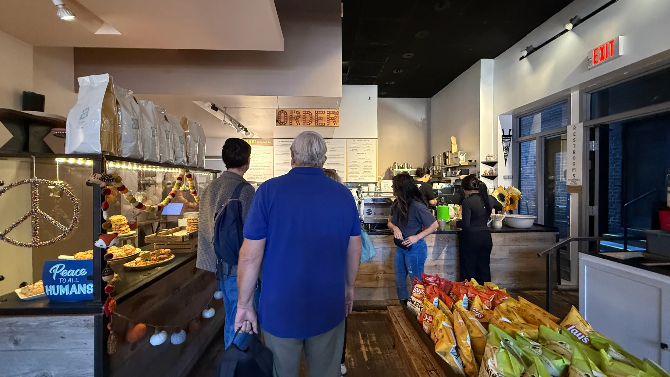 Inside Henry & The Fish: customers queue at a wood-topped counter under a marquee ORDER sign while staff work the espresso machine