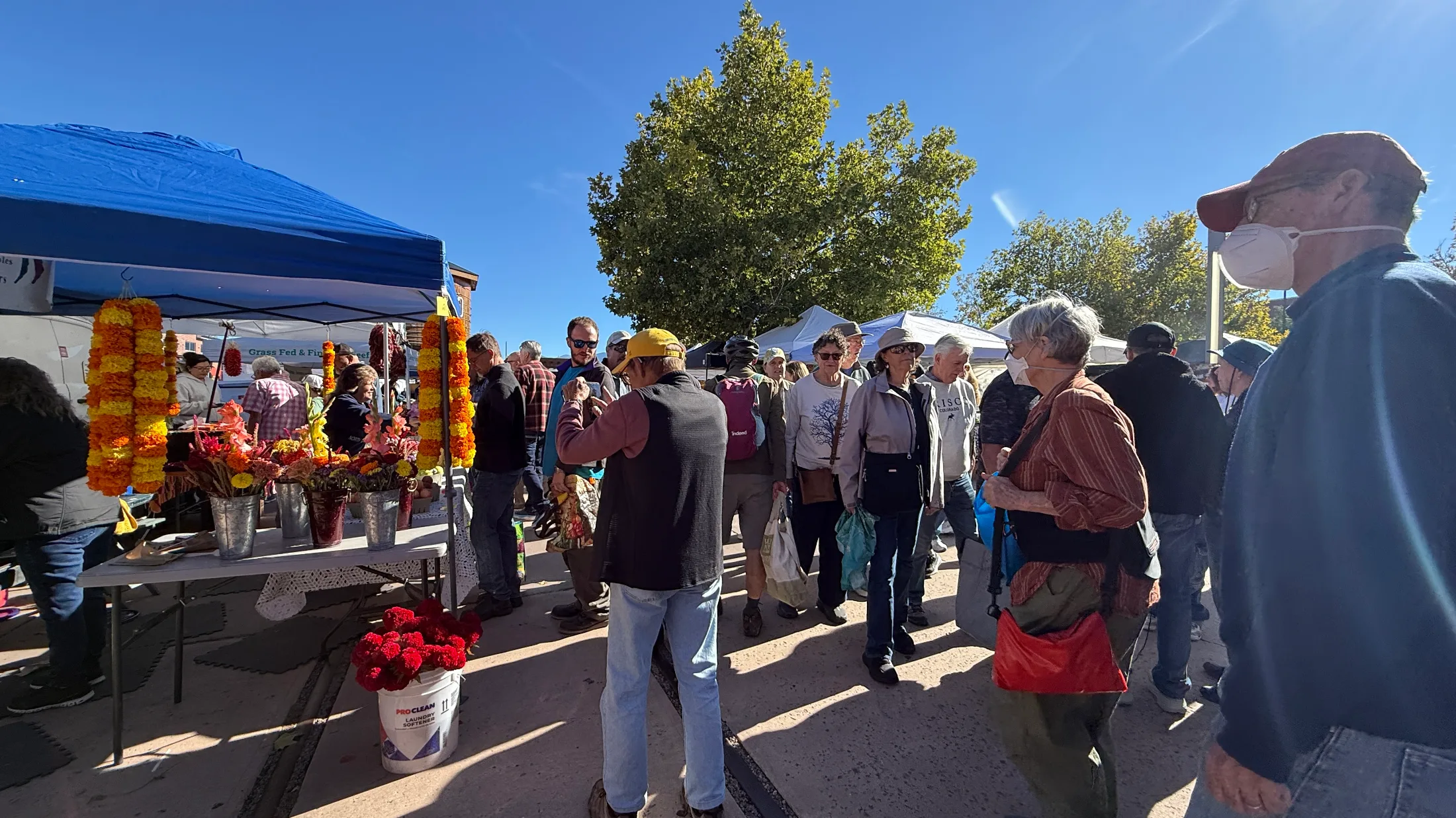 Marigold garlands and cut flowers at a flower vendor booth, with a dense Saturday crowd behind