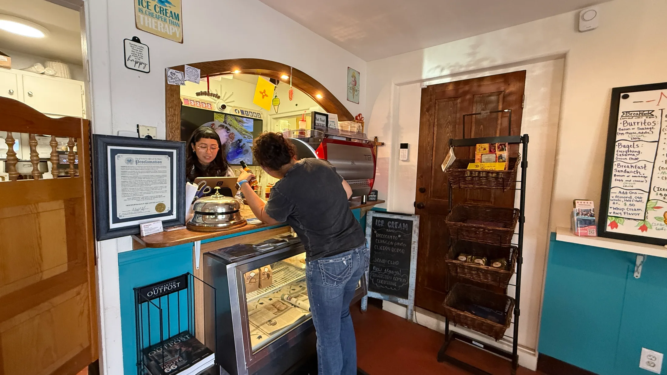 Counter service at Santa Fe Biscochito Company, with an ice cream case, a staff member at the register, and a chalkboard ice cream menu on the wall