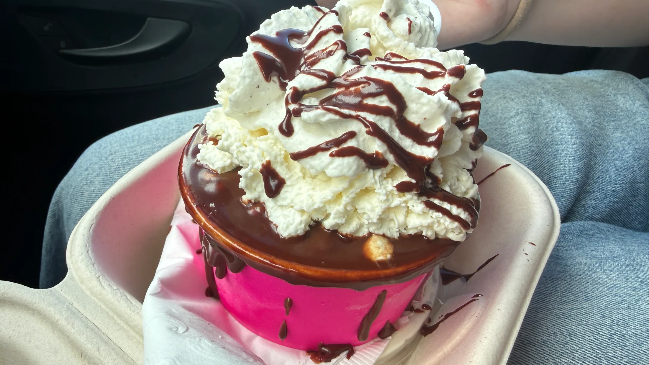 Kakawa brownie sundae to-go in a pink cup overflowing with whipped cream and chocolate sauce drizzle
