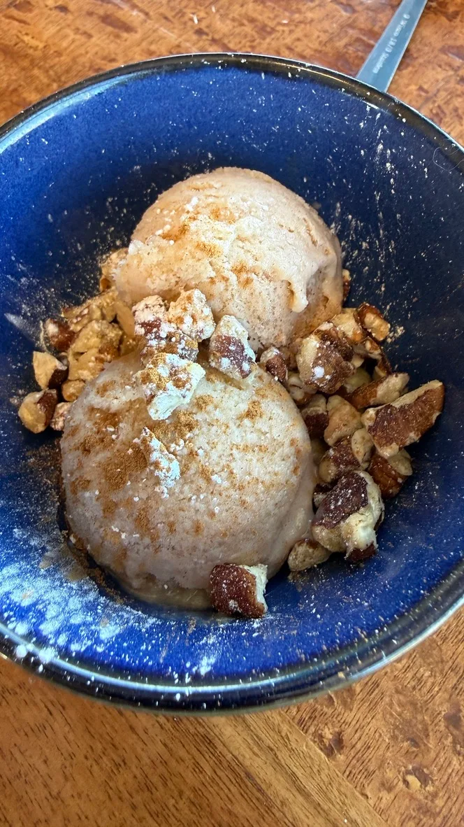 Two scoops of cinnamon-dusted ice cream with crushed walnuts in a deep blue ceramic bowl