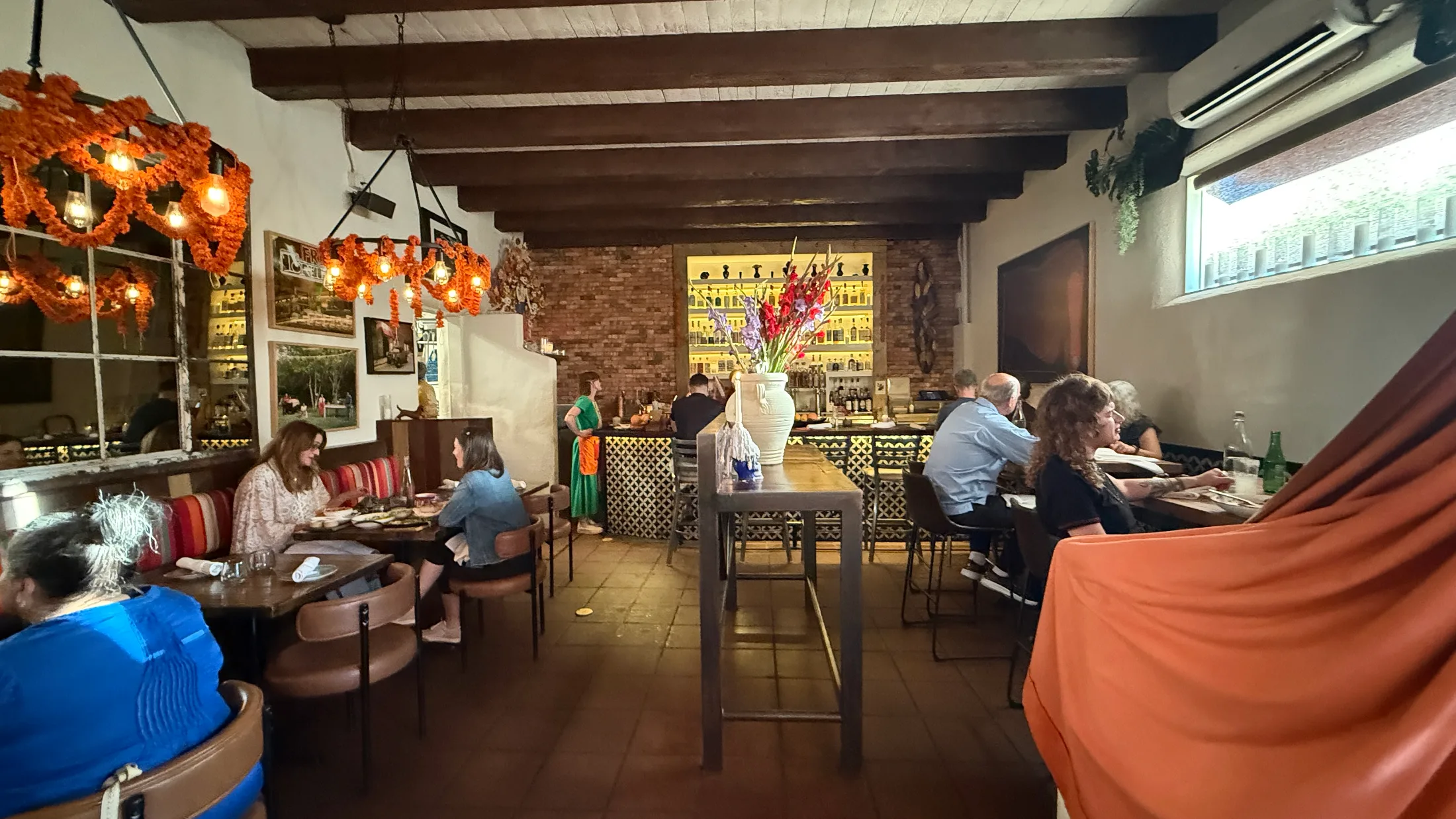 Paloma dining room interior β exposed vigas, marigold-wrapped chandelier, brick bar backlit with agave spirits
