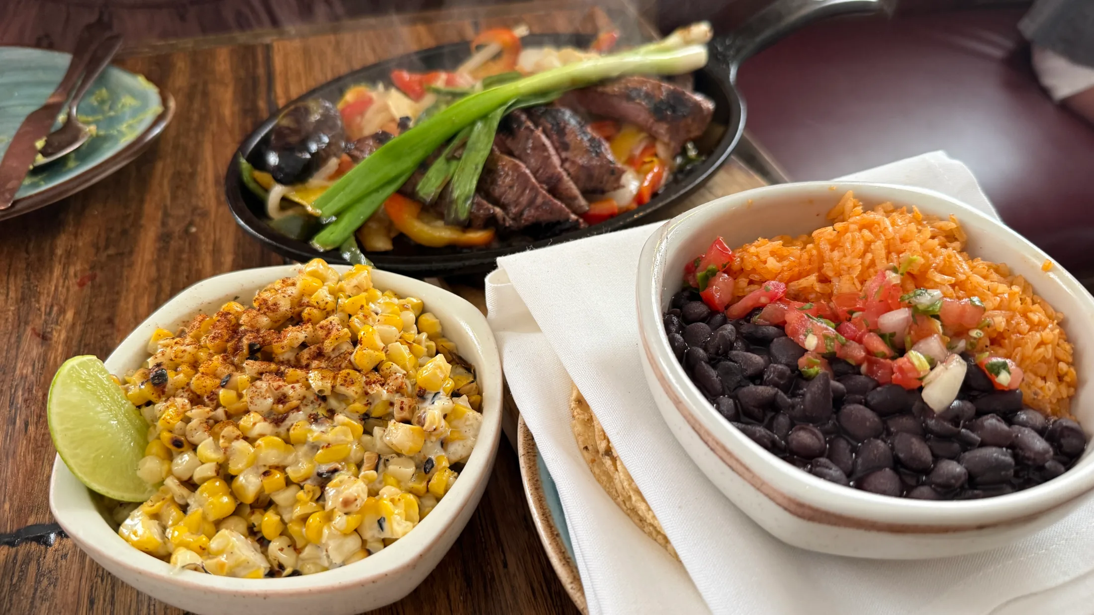 Paloma dinner spread β sizzling steak fajita skillet, elote off the cob with crema and chili, black beans and Spanish rice