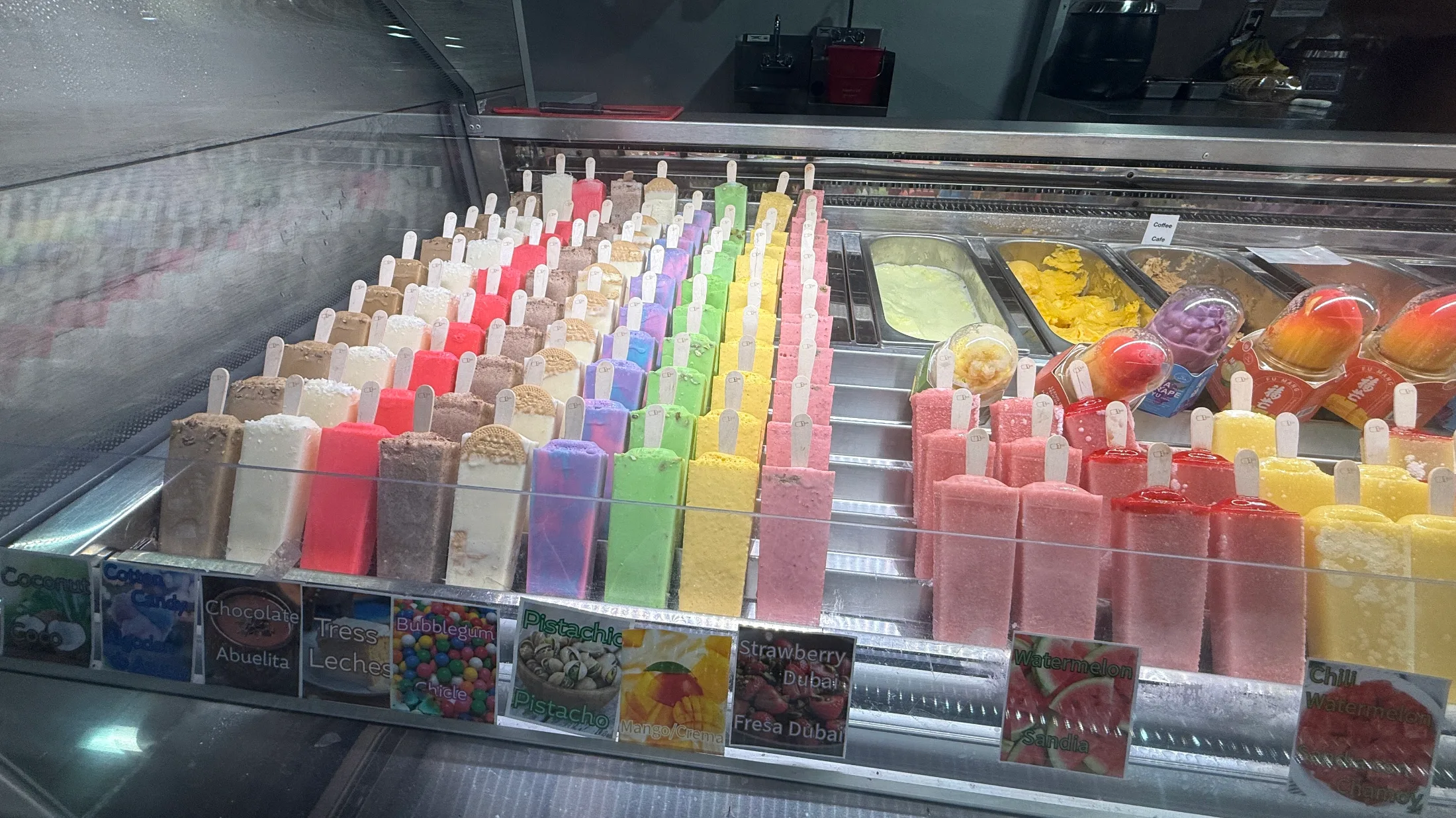 A paleta dipped in white chocolate with drizzled streaks, held up in front of The Paleta Bar storefront