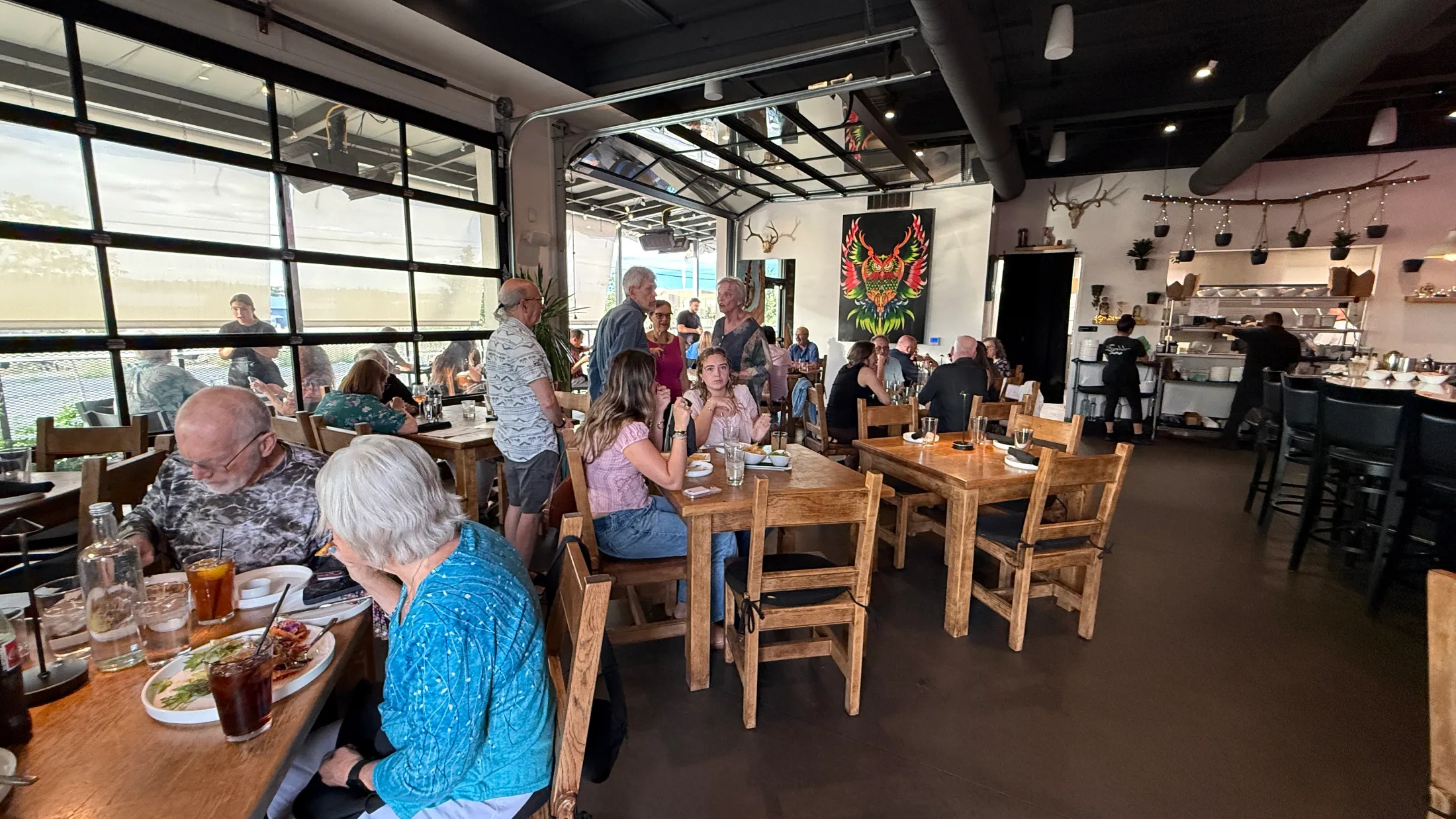 Escondido dining room — wood tables, owl mural, antler mounts, glass garage wall open to the street
