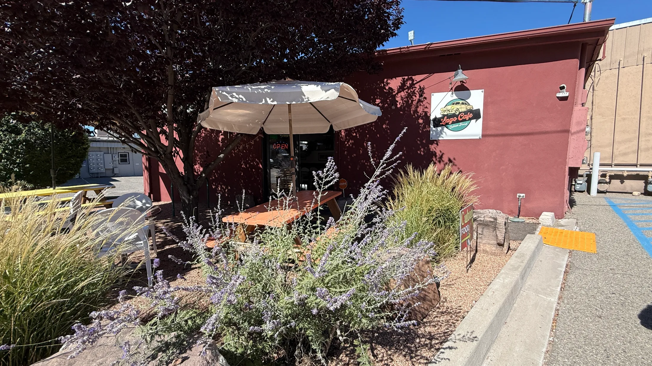 Lago Cafe patio with a wooden picnic table, sage and ornamental grasses, and a red stucco exterior