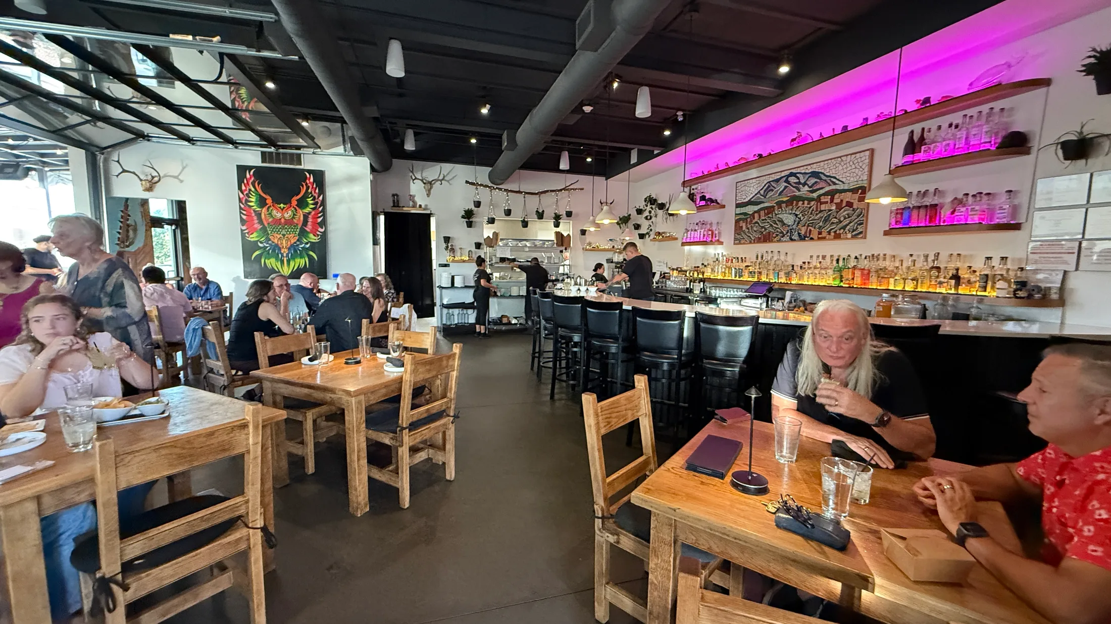 Escondido interior at peak dinner service — full room, bar under pink light, owl mural, open kitchen