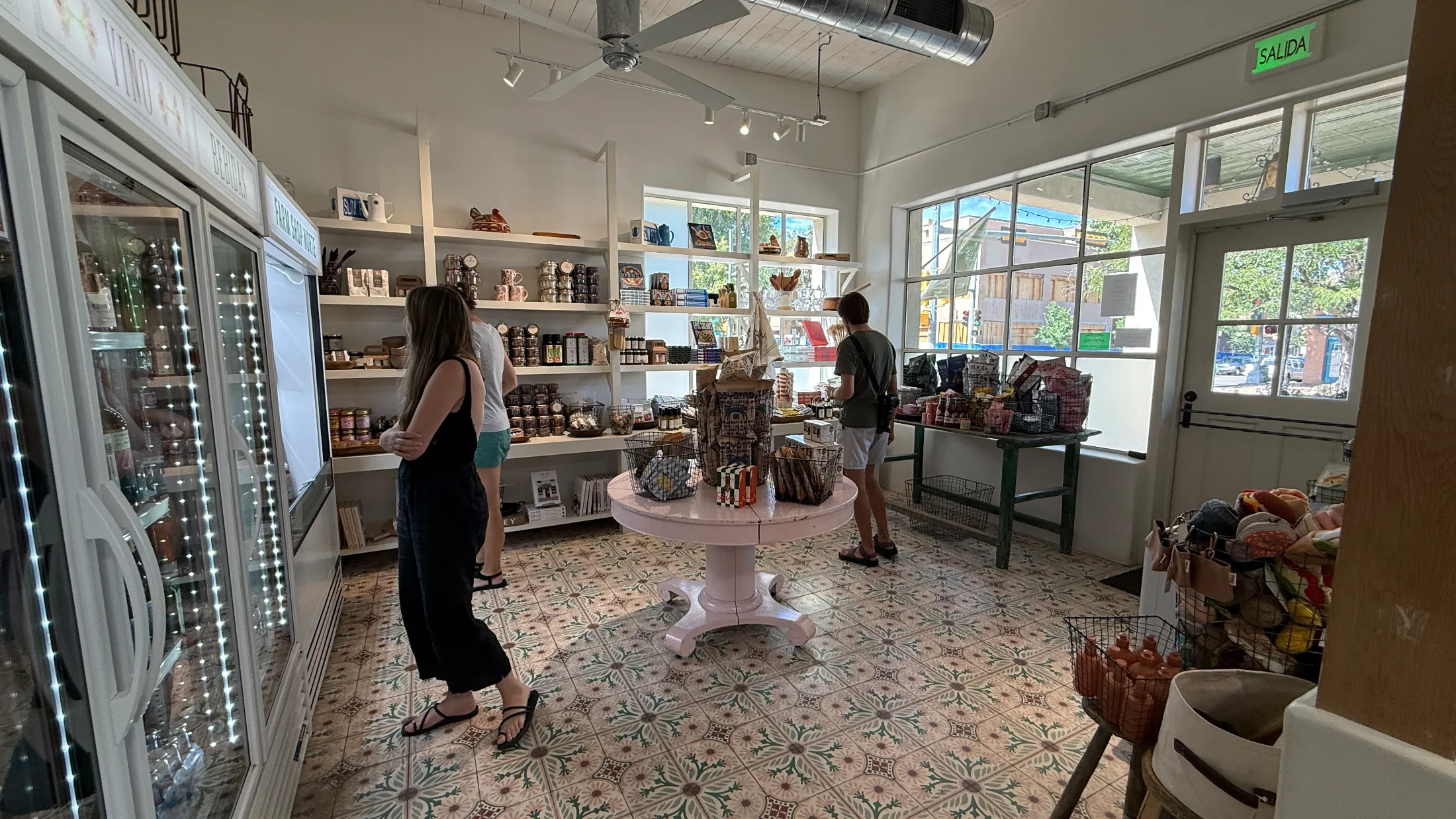 Back room of Farm Shop Norte with encaustic tile floors, wine and beverage coolers labeled Vino and Bebida, and shoppers browsing shelves of local pantry goods