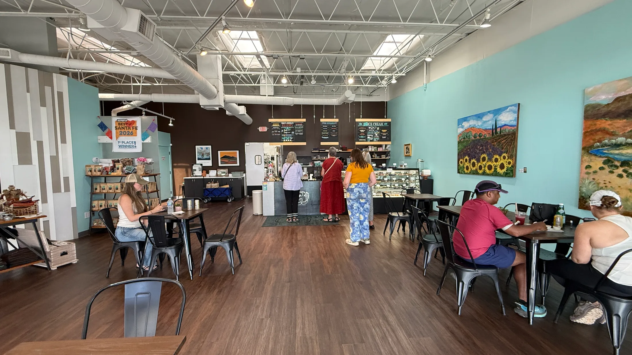 Kakawa dining room with local New Mexico landscape paintings on teal walls and guests at black metal tables