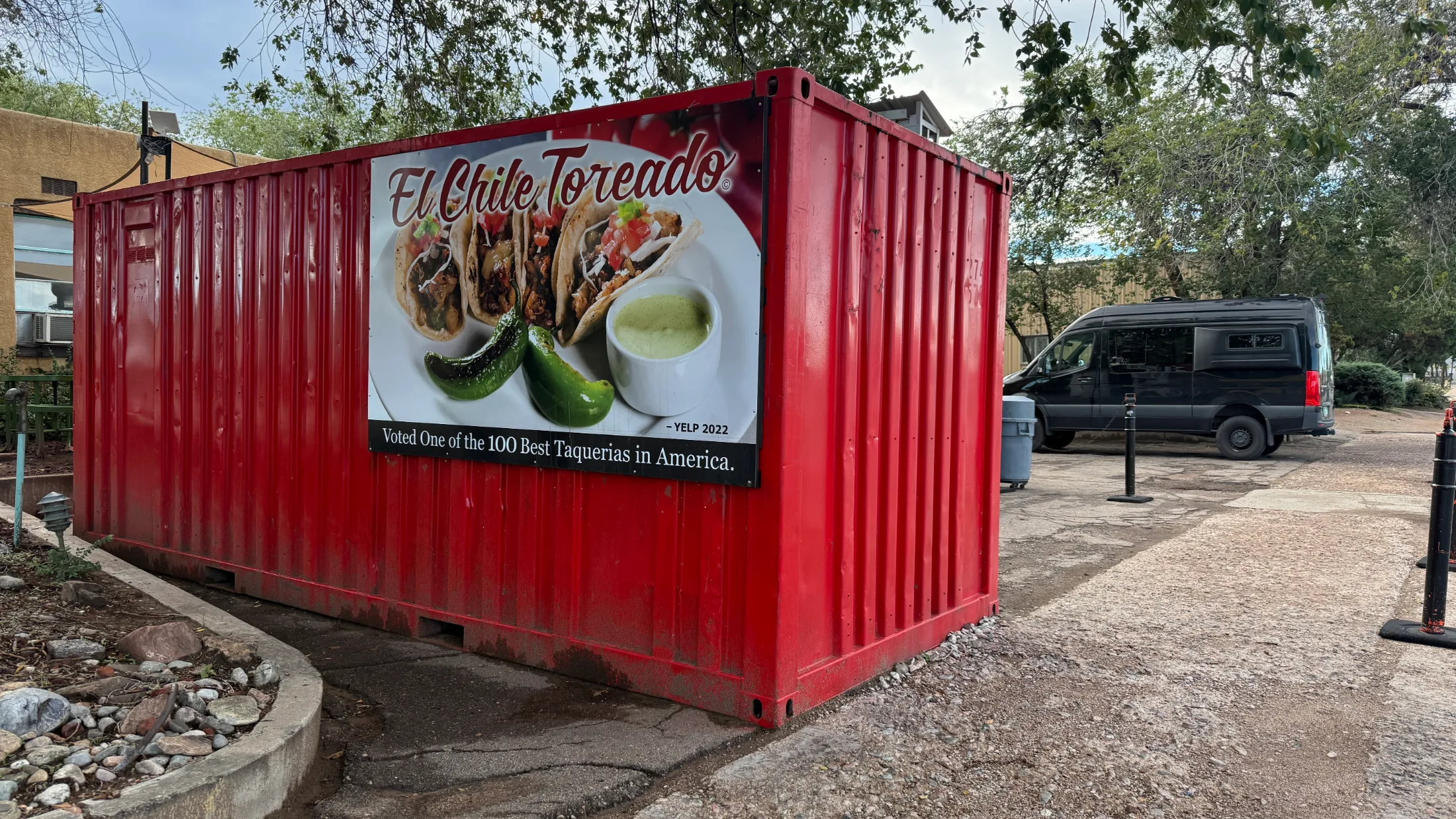 A breakfast burrito cut in half and held up, showing egg, potato, and meat filling, with a side of green salsa