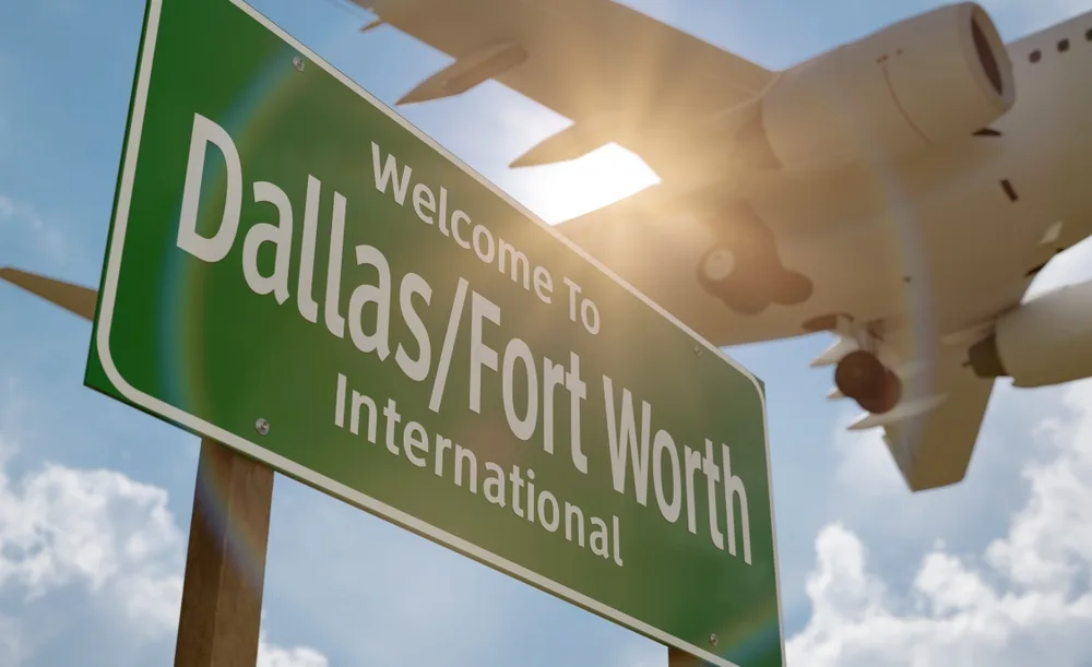 Dallas/Fort Worth International Airport welcome sign with airplane overhead against bright sky