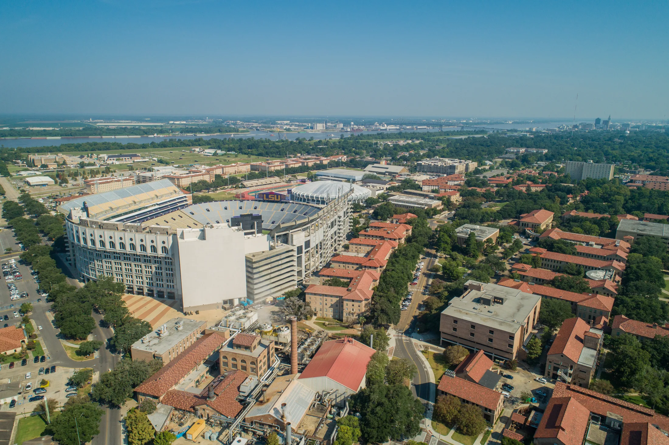 Aerial view of Tiger Stadium and the red-roofed LSU campus with the Mississippi River in the background