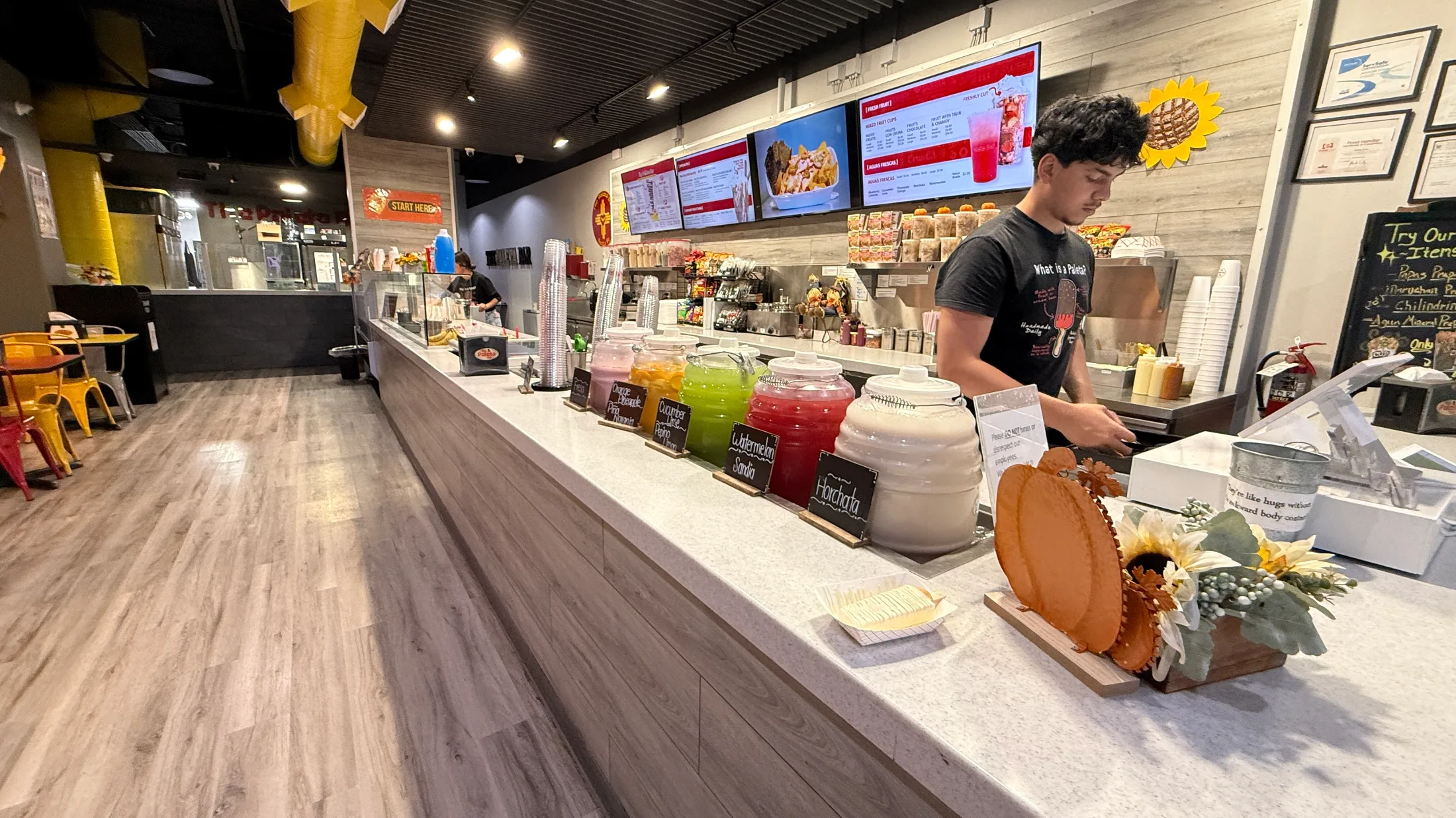 The Paleta Bar counter with aguas frescas in glass jars, including watermelon and horchata, and a staff member working behind the bar
