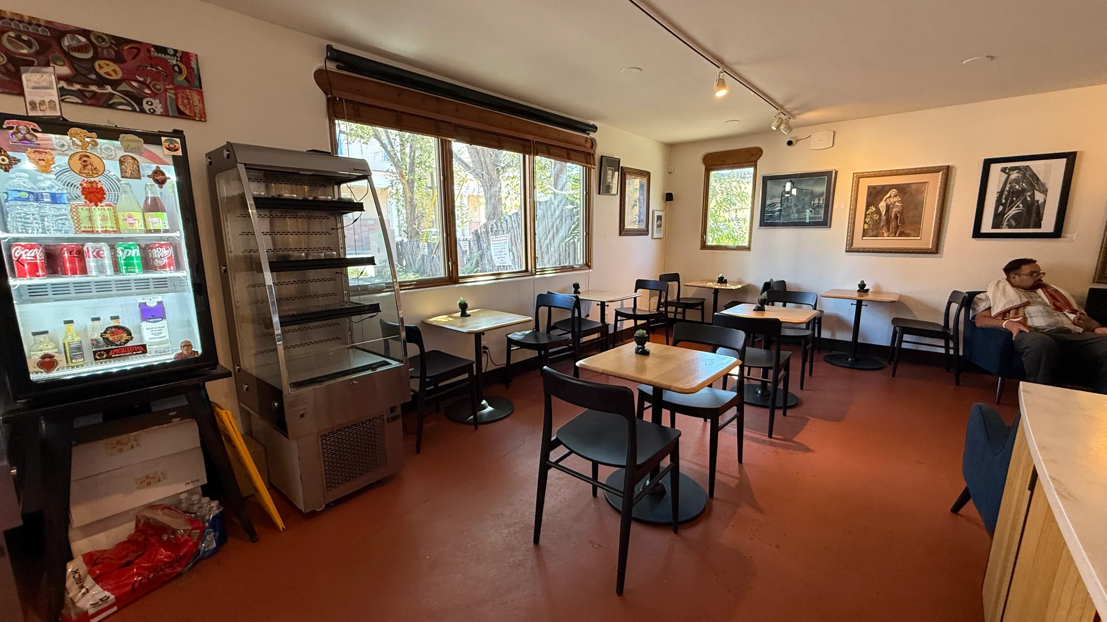 Dining room inside Santa Fe Biscochito Company, with cafe tables, framed artwork, and a beverage cooler along the wall