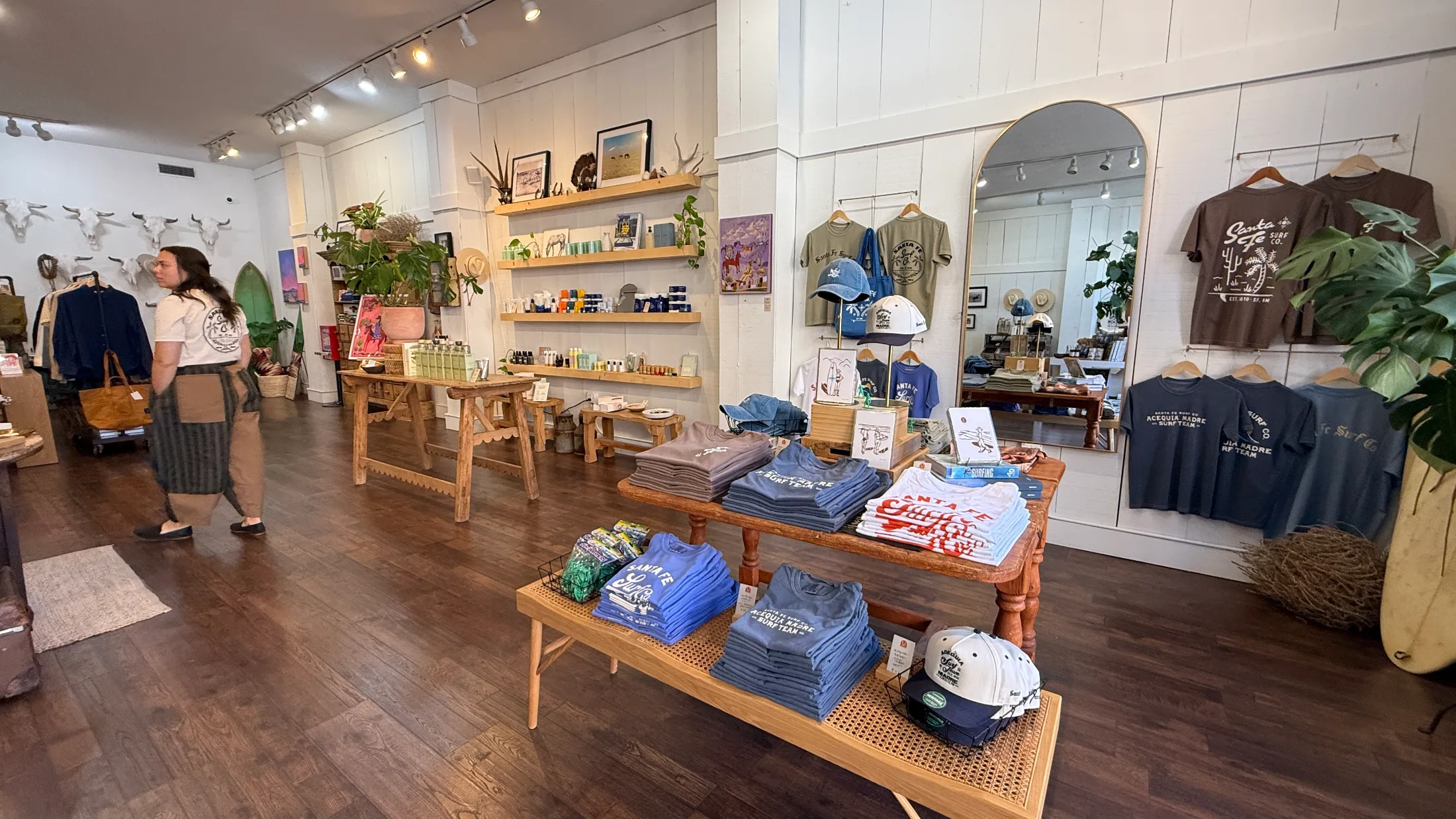 Apparel section of High Noon General Store with Santa Fe Surf Co. and Acequia Madre Surf Team tees stacked on wooden tables