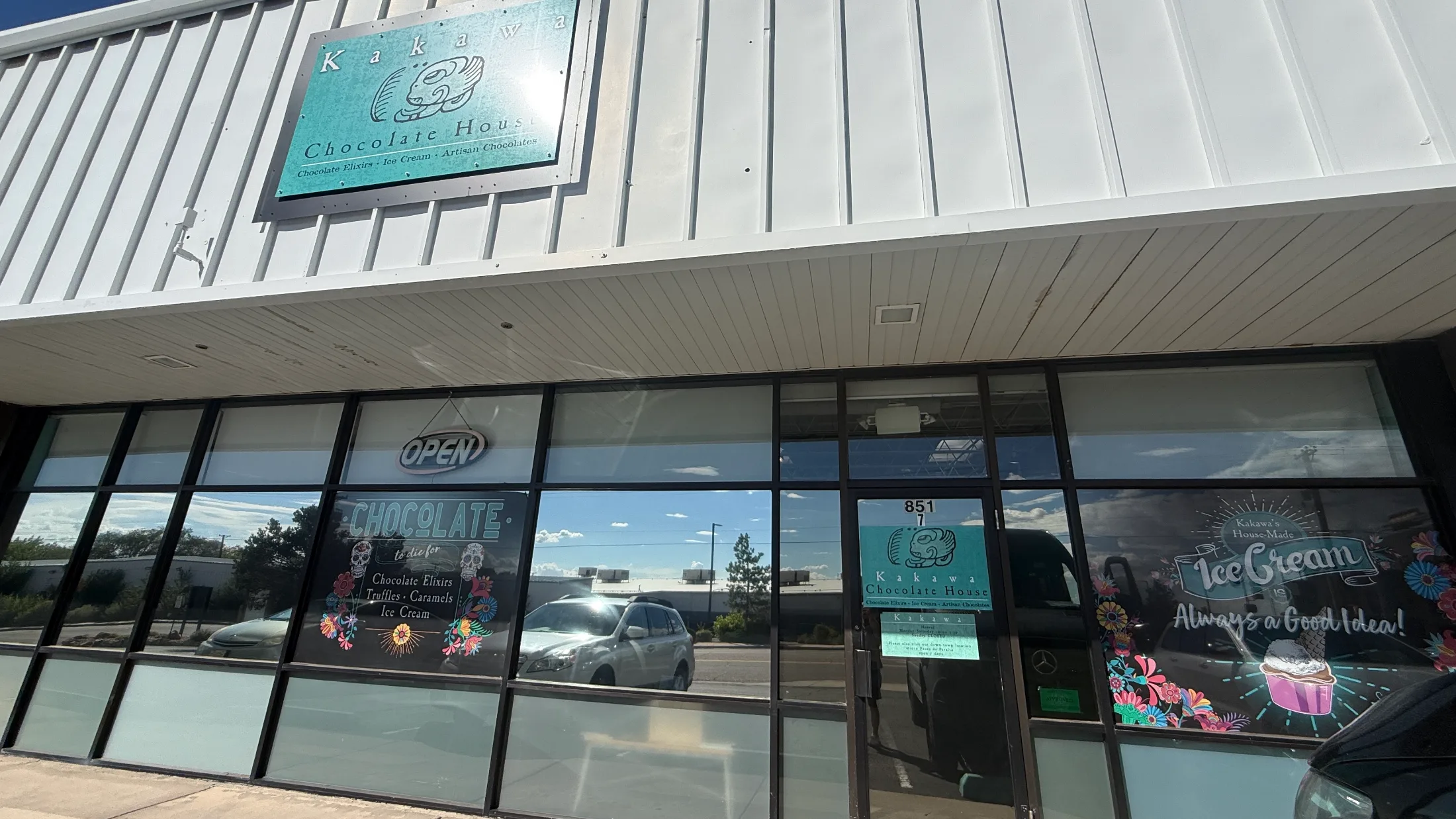 Exterior of Kakawa Chocolate House with teal signage, decorative window lettering for chocolate elixirs, truffles, caramels, and ice cream