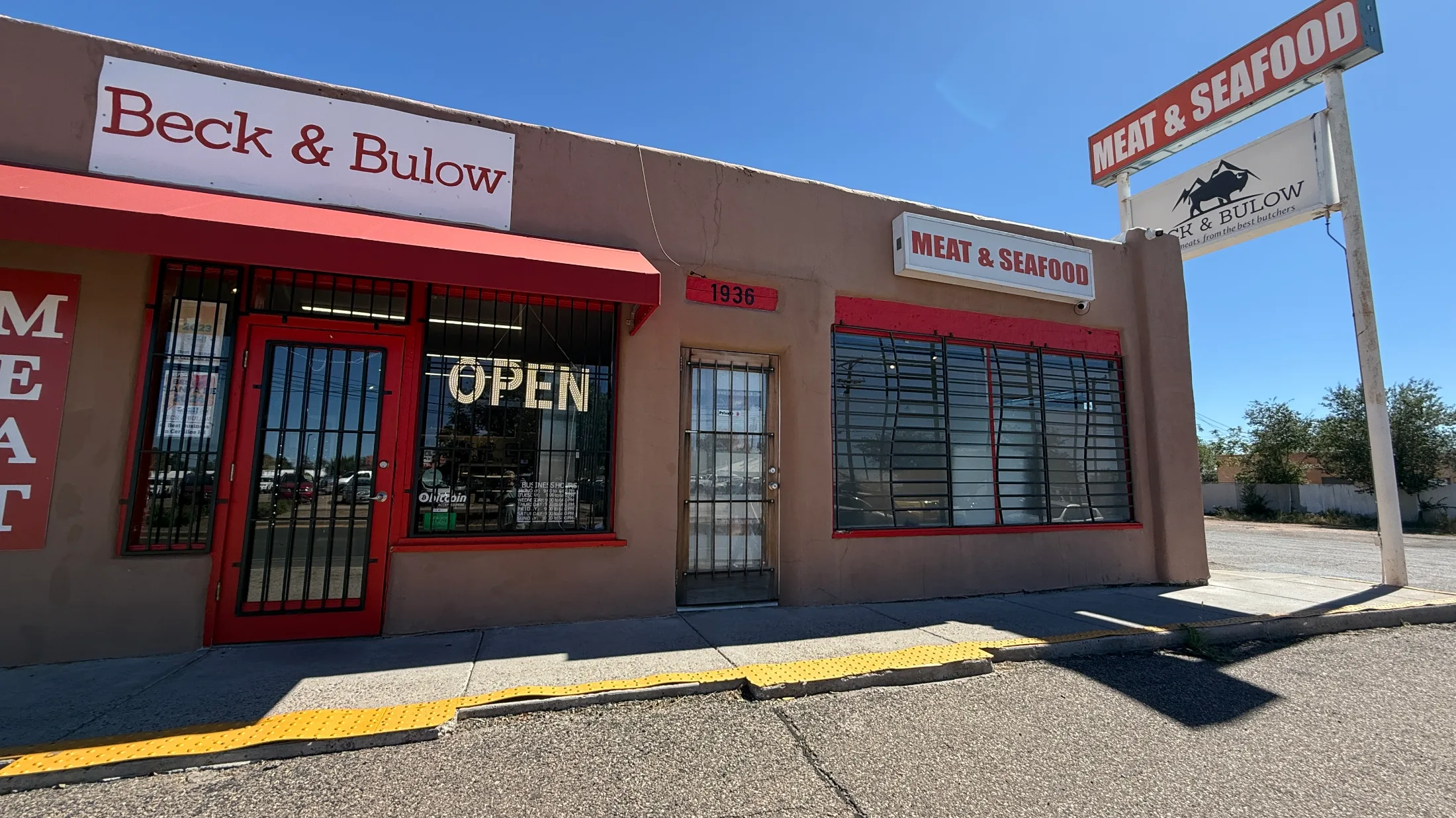 Exterior of Beck and Bulow on Cerrillos Road with red and white signage reading Meat and Seafood and an OPEN sign in the window