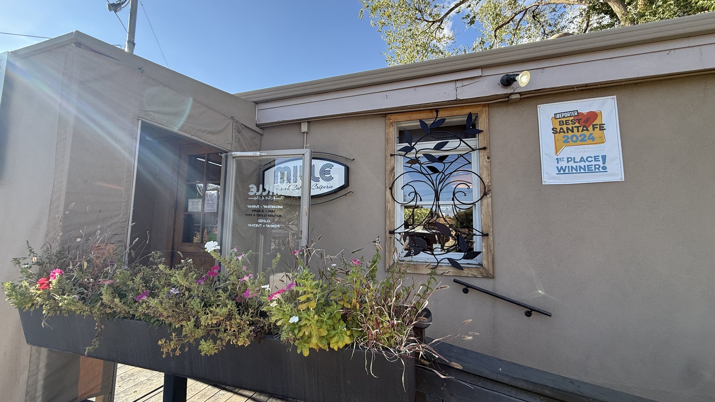 The cafe entrance with a Mille French Cafe & Creperie sign, a flower box and a window with a black iron leaf design