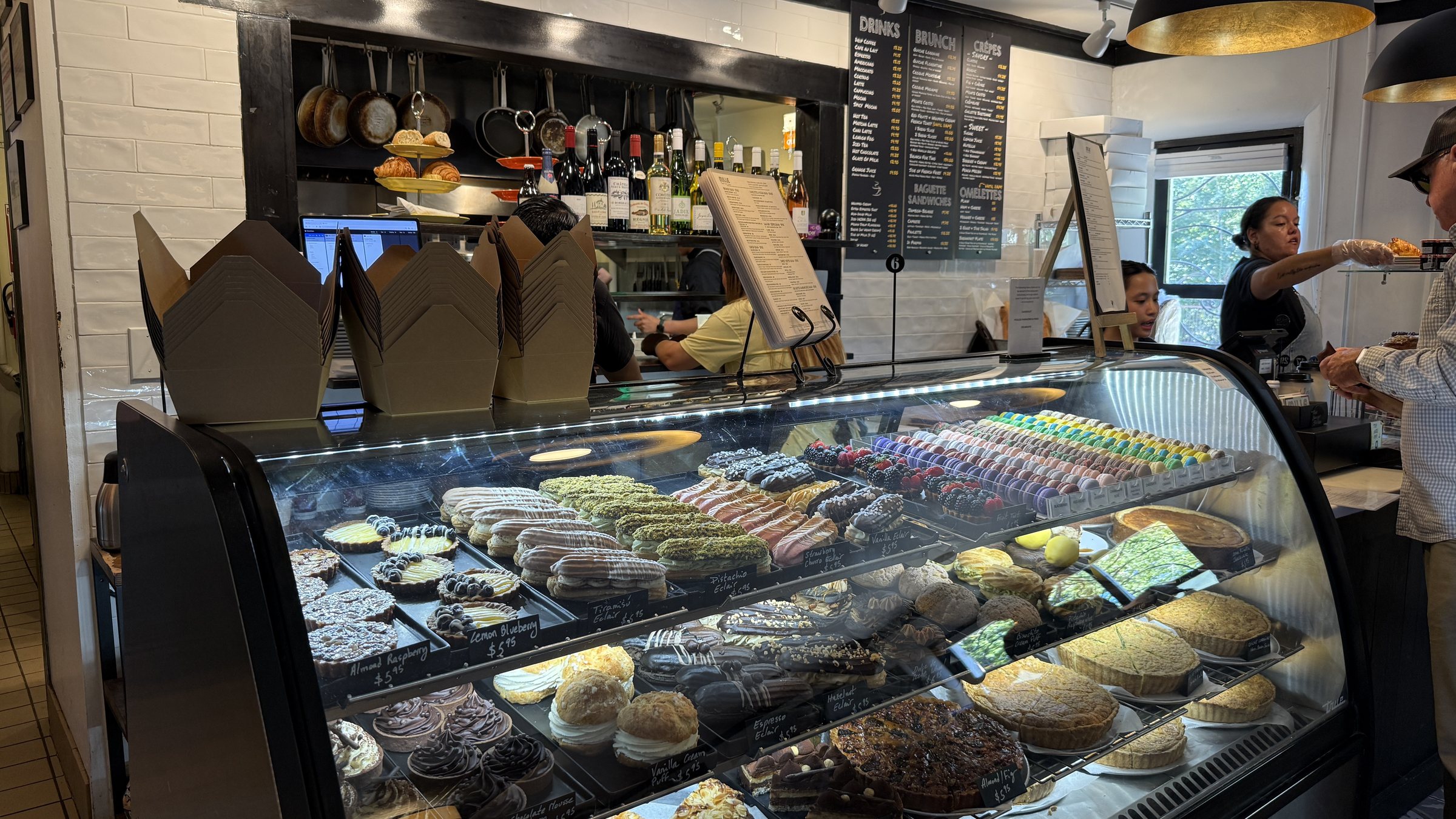 A curved glass pastry case with rows of colorful macarons, eclairs, cream puffs and fruit tarts