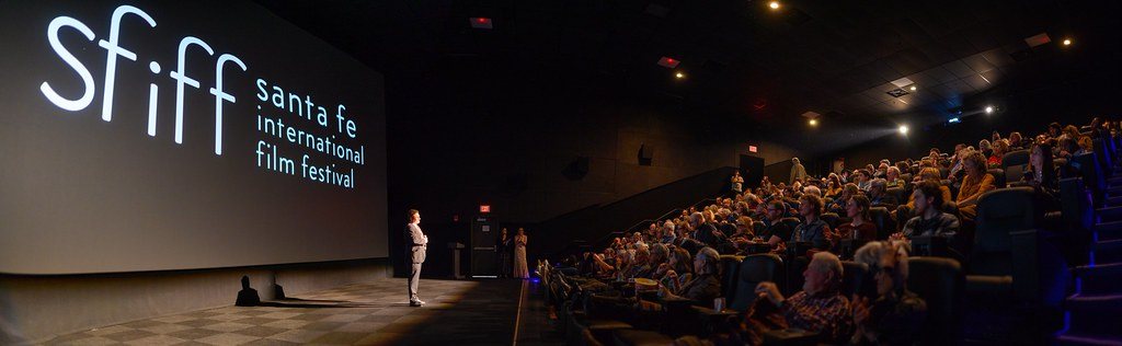 Audience seated in a dark cinema facing a bright screen