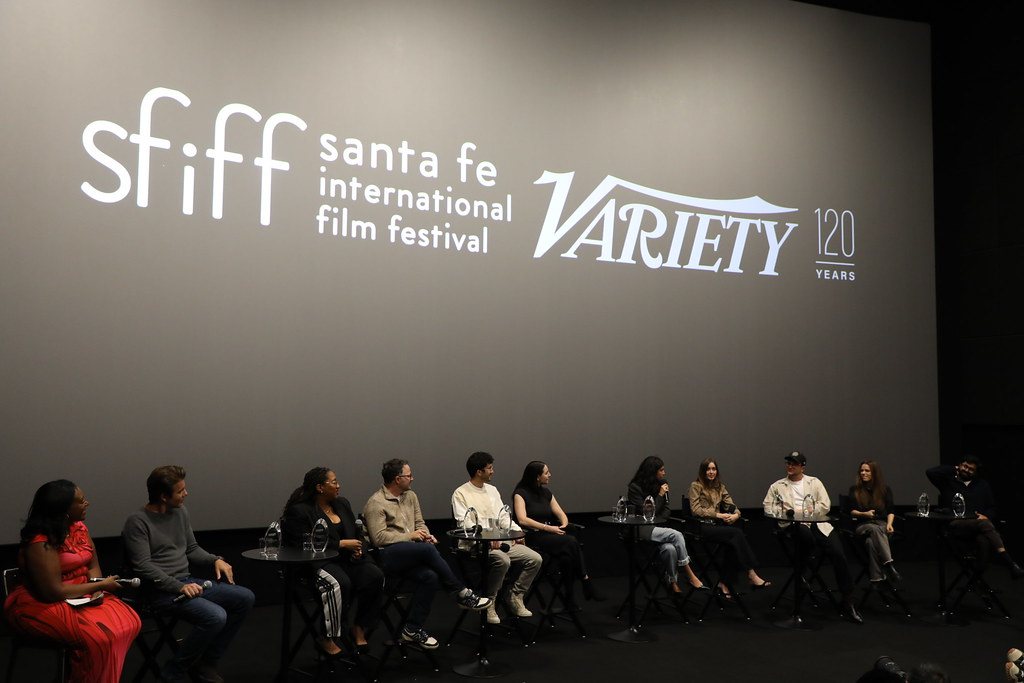 People seated on a stage under large white logos on a screen