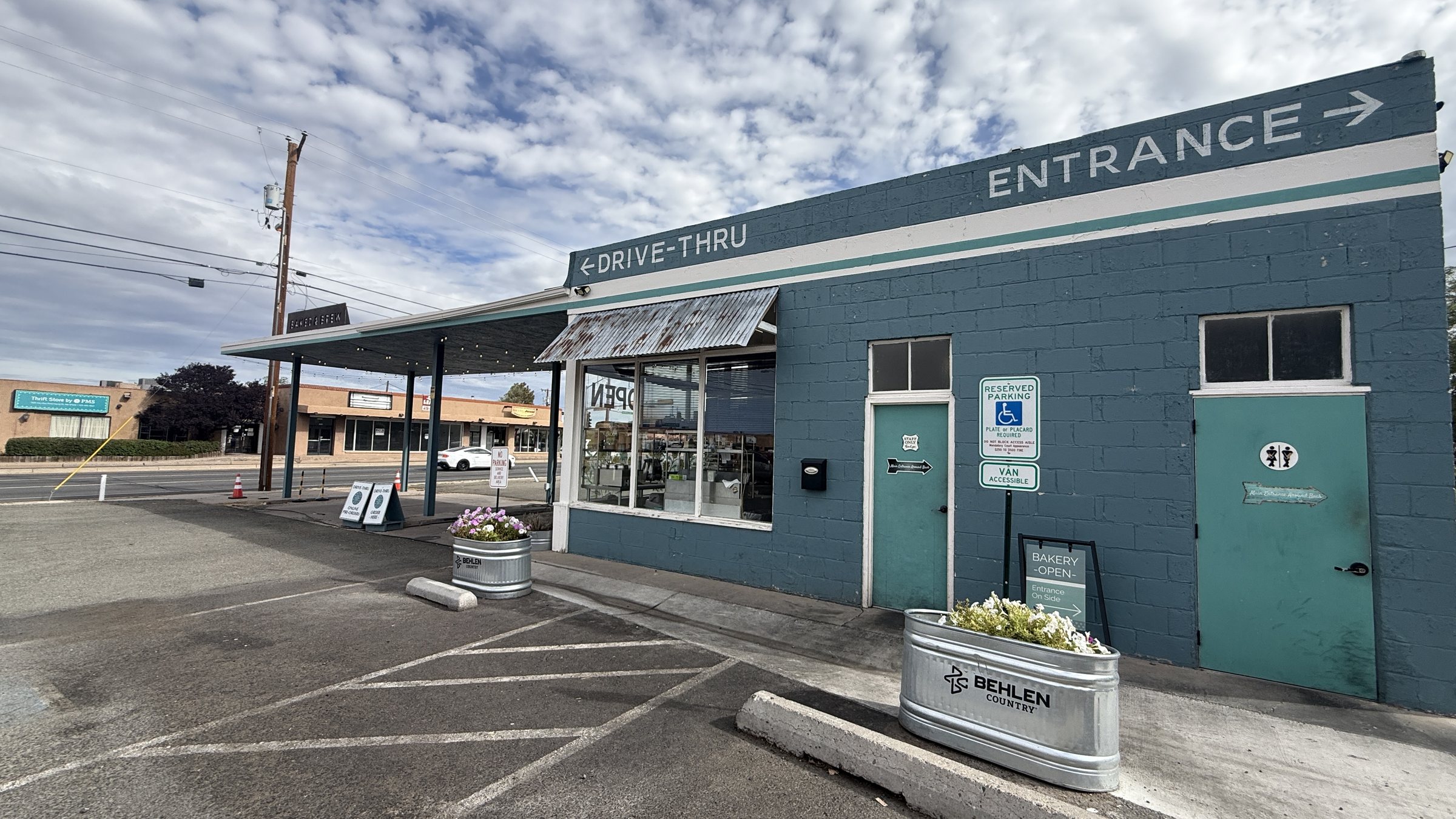 Painted DRIVE-THRU and ENTRANCE arrows on the teal block building at Baked and Brew, with planters out front
