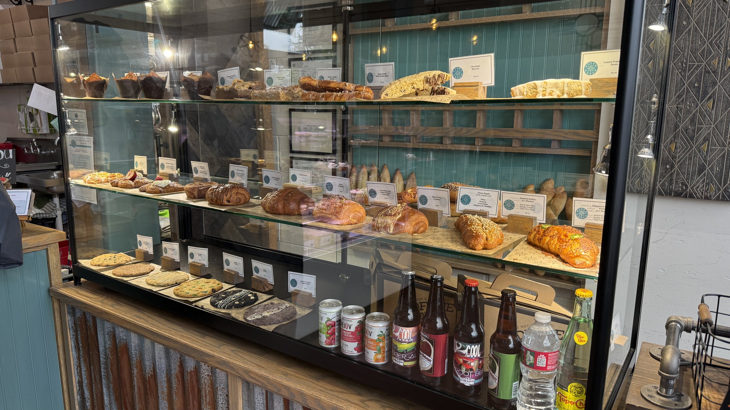 Croissants, cookies and braided loaves above glass-bottle sodas at Baked and Brew