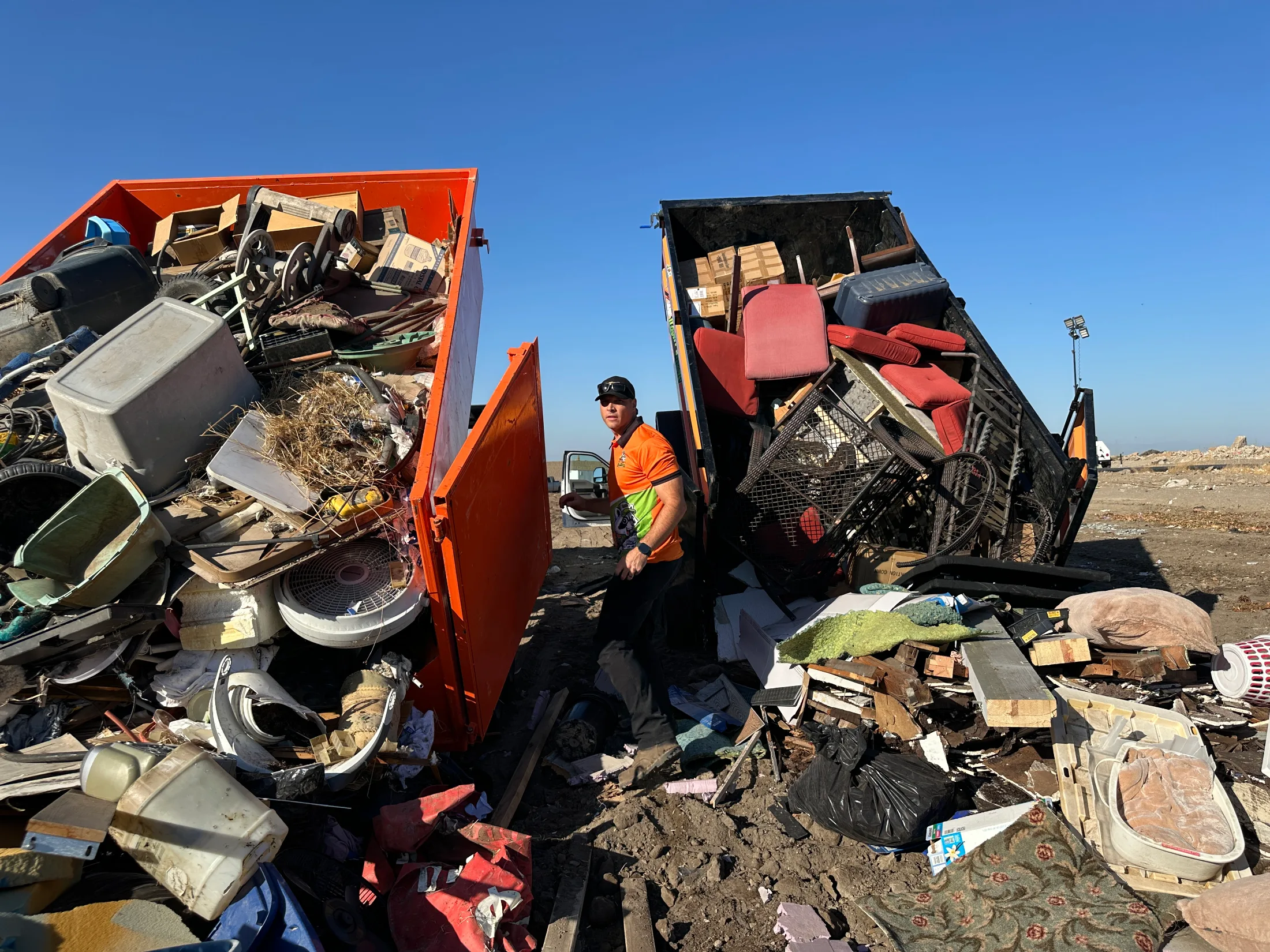 Andrew Haskins standing between two overflowing dump trailers at a disposal site, showing the scale of a large junk removal haul